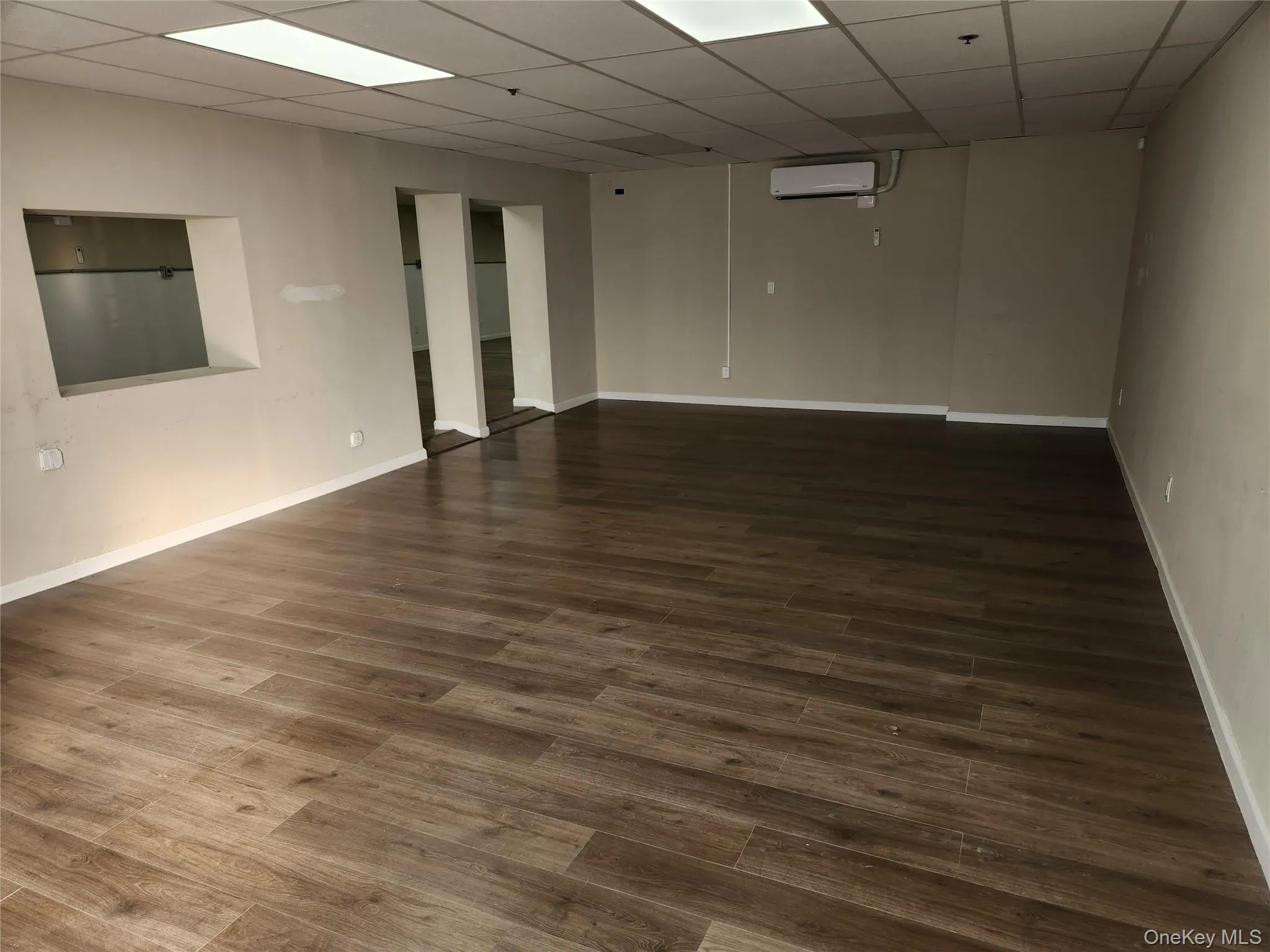 Spare room with a paneled ceiling, dark wood-style floors, and an AC wall unit Spare room with a paneled ceiling, dark wood-style floors, and an AC wall unit