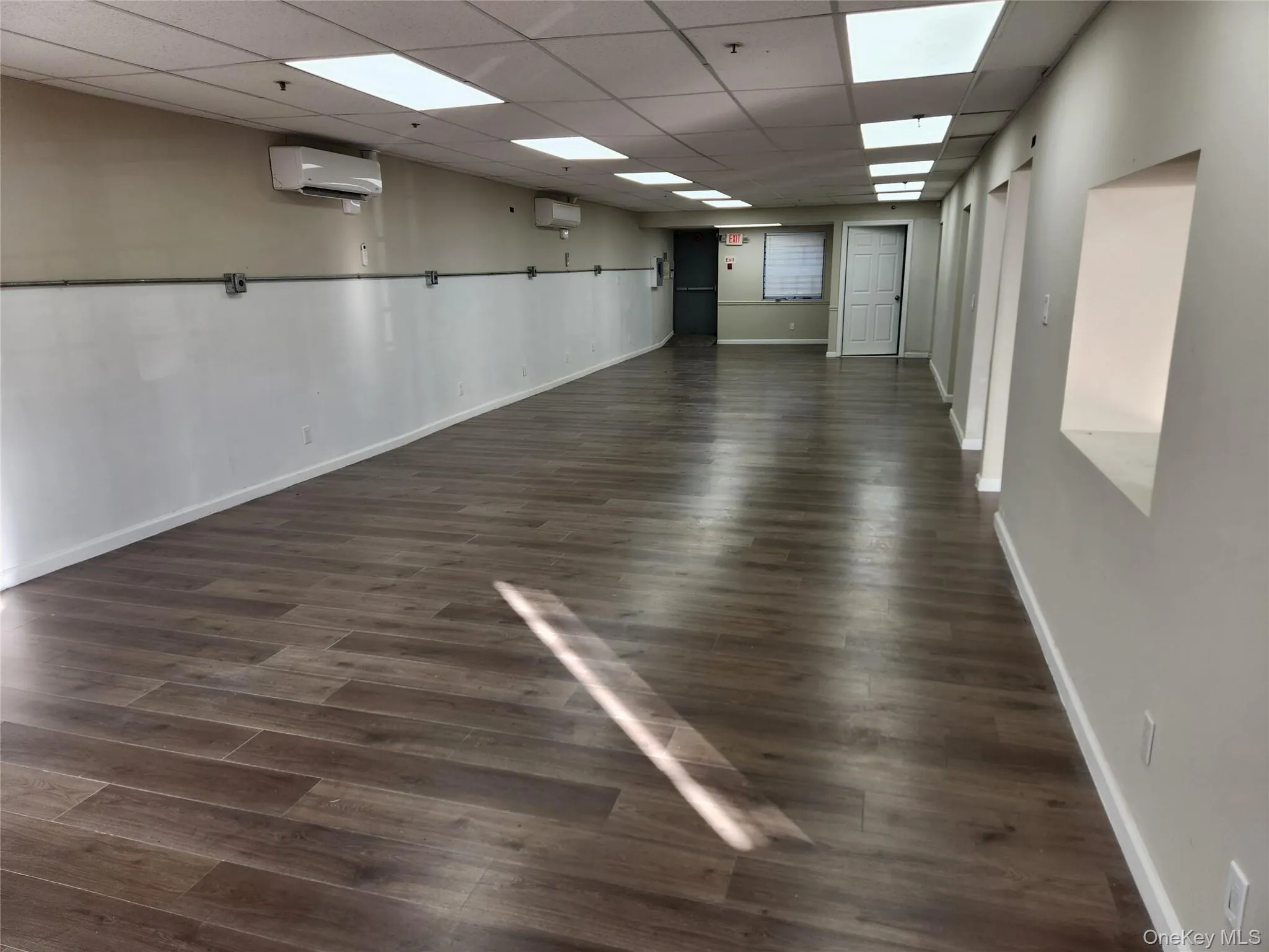 Unfurnished room with a drop ceiling, dark wood-style flooring, and an AC wall unit Unfurnished room with a drop ceiling, dark wood-style flooring, and an AC wall unit