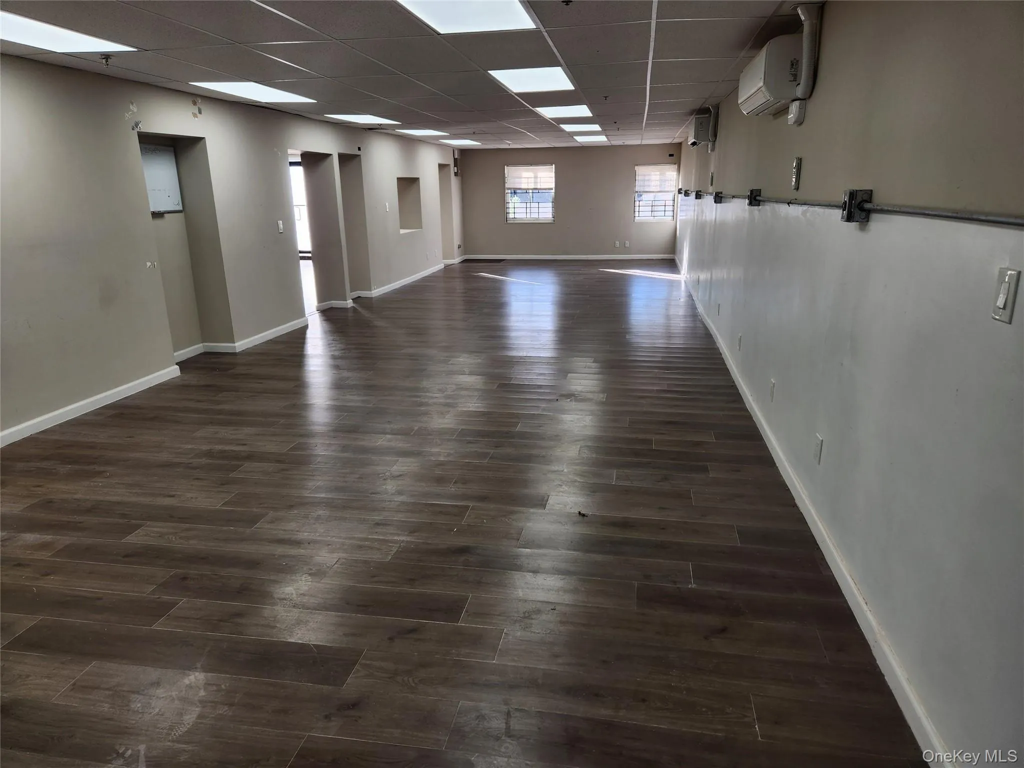 Unfurnished room featuring dark wood finished floors, a drop ceiling, and a wall mounted AC Unfurnished room featuring dark wood finished floors, a drop ceiling, and a wall mounted AC