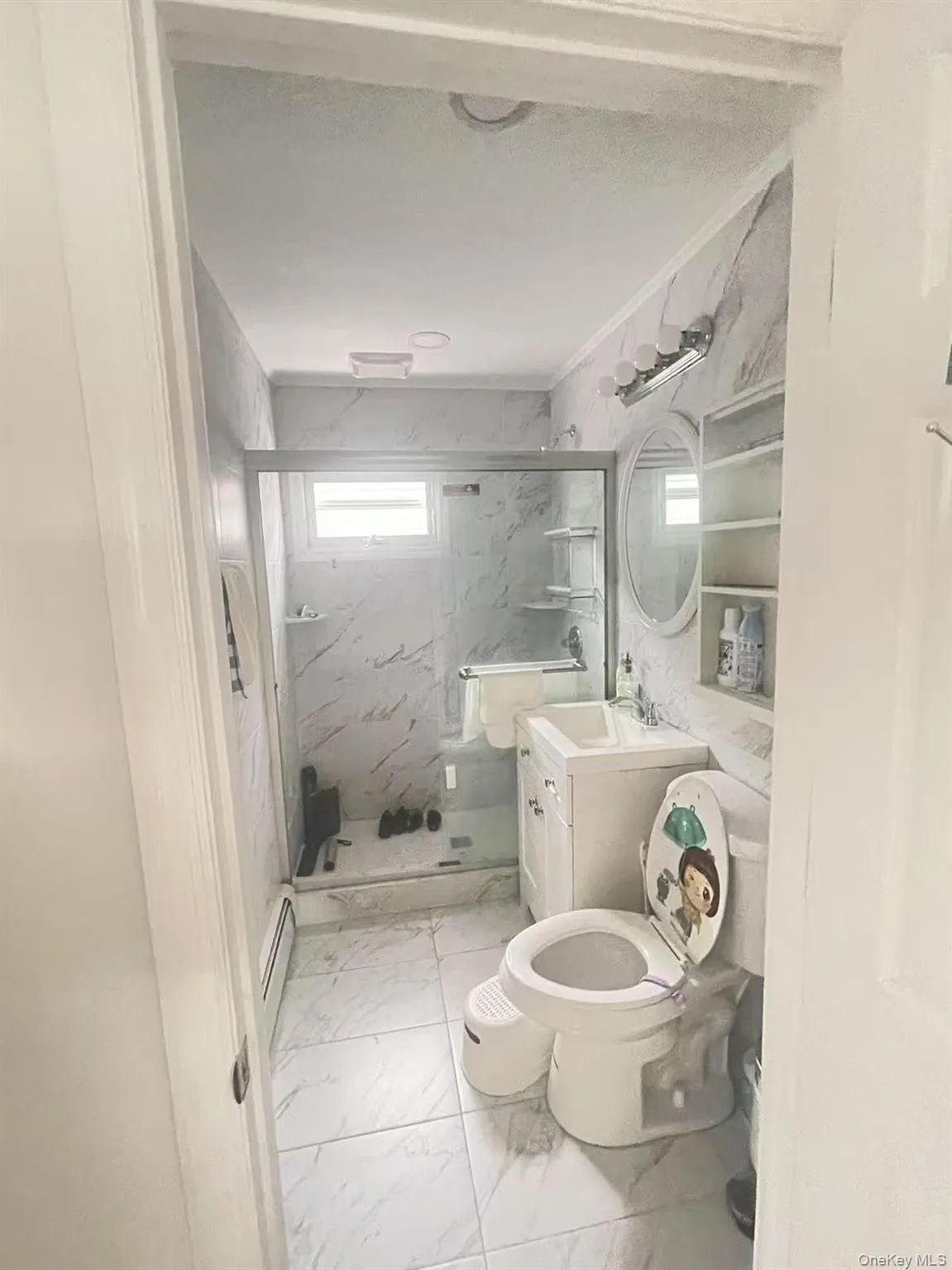 Full bath with light marble finish flooring, a marble finish shower, vanity, and ornamental molding Full bath with light marble finish flooring, a marble finish shower, vanity, and ornamental molding
