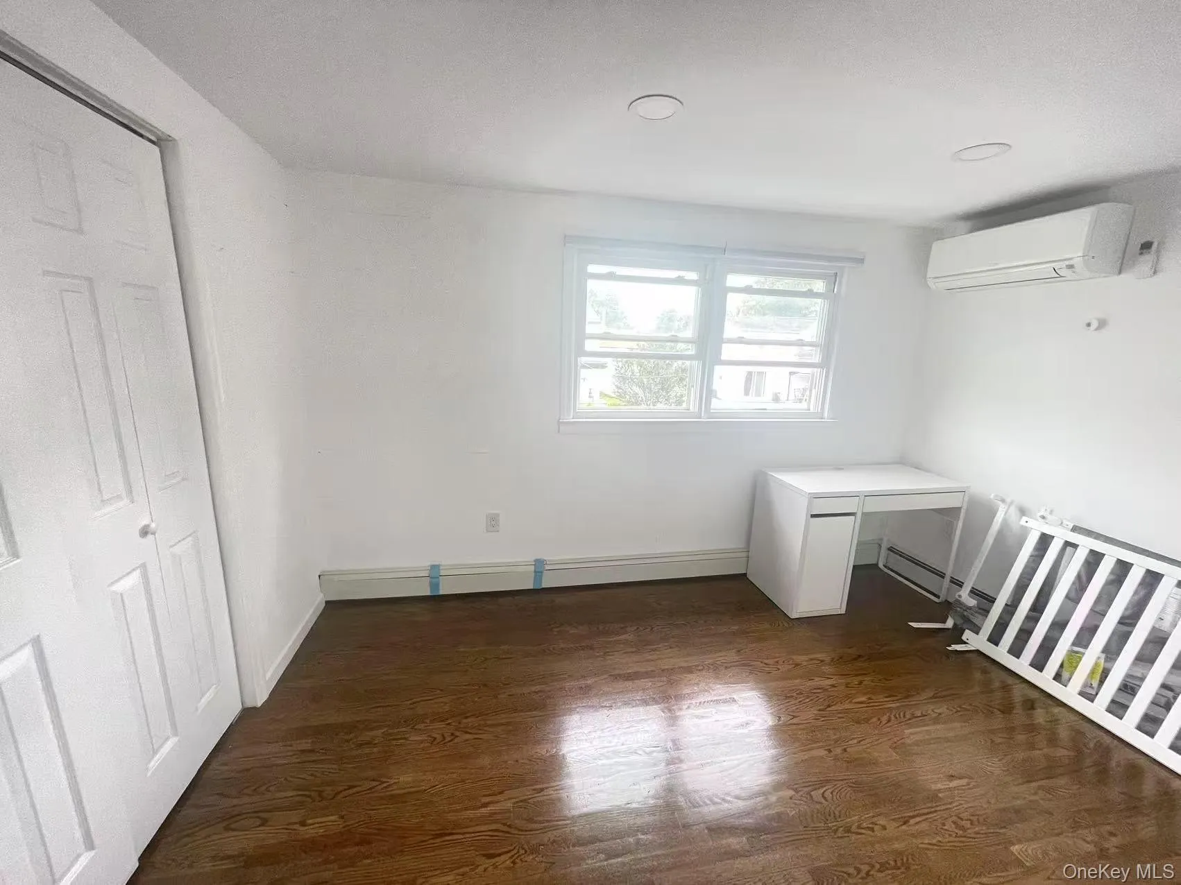 Unfurnished bedroom with dark wood finished floors, a wall mounted AC, and a baseboard radiator Unfurnished bedroom with dark wood finished floors, a wall mounted AC, and a baseboard radiator