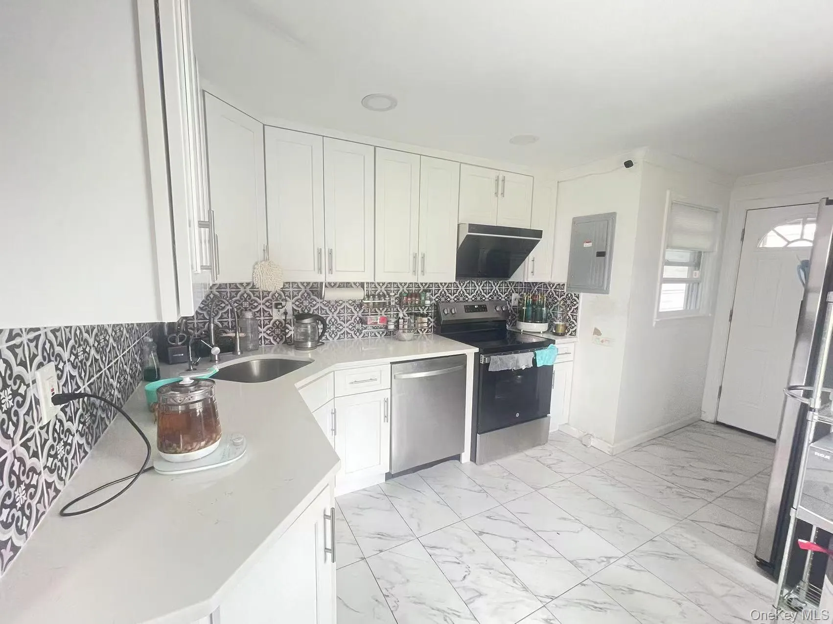 Kitchen with white cabinets, decorative backsplash, appliances with stainless steel finishes, light marble finish floors, and electric panel Kitchen with white cabinets, decorative backsplash, appliances with stainless steel finishes, light marble finish floors, and electric panel