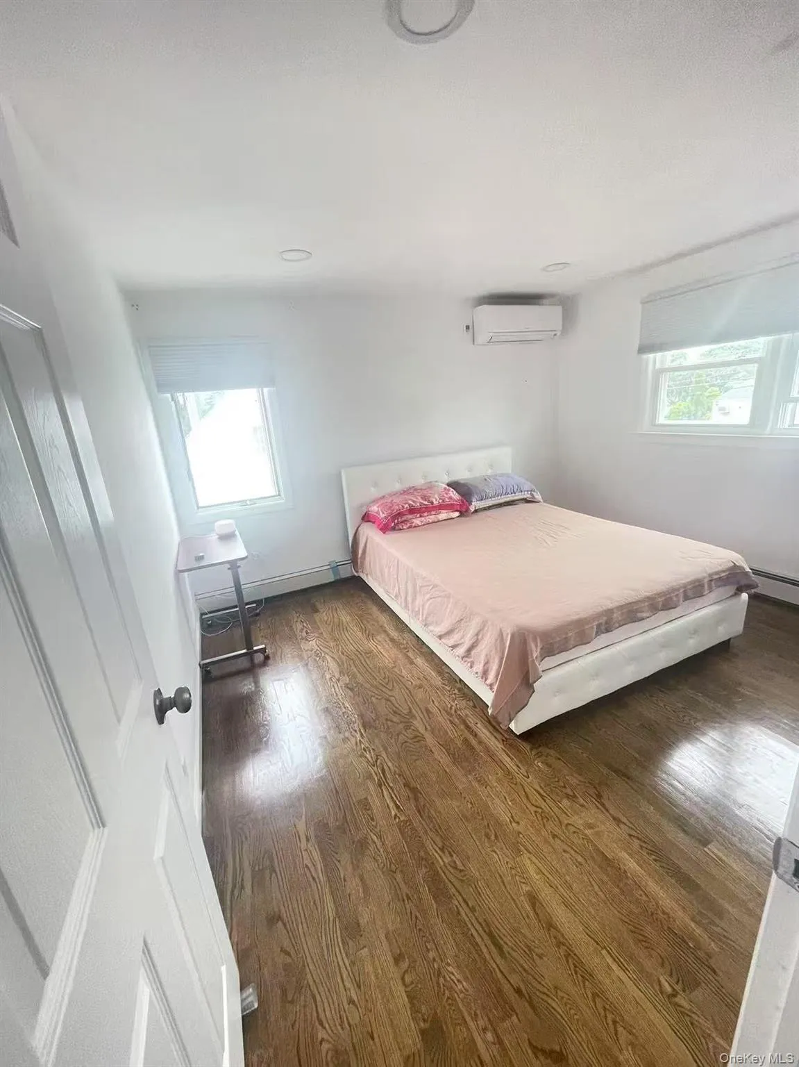 Bedroom with multiple windows, wood finished floors, a baseboard heating unit, and a wall unit AC Bedroom with multiple windows, wood finished floors, a baseboard heating unit, and a wall unit AC