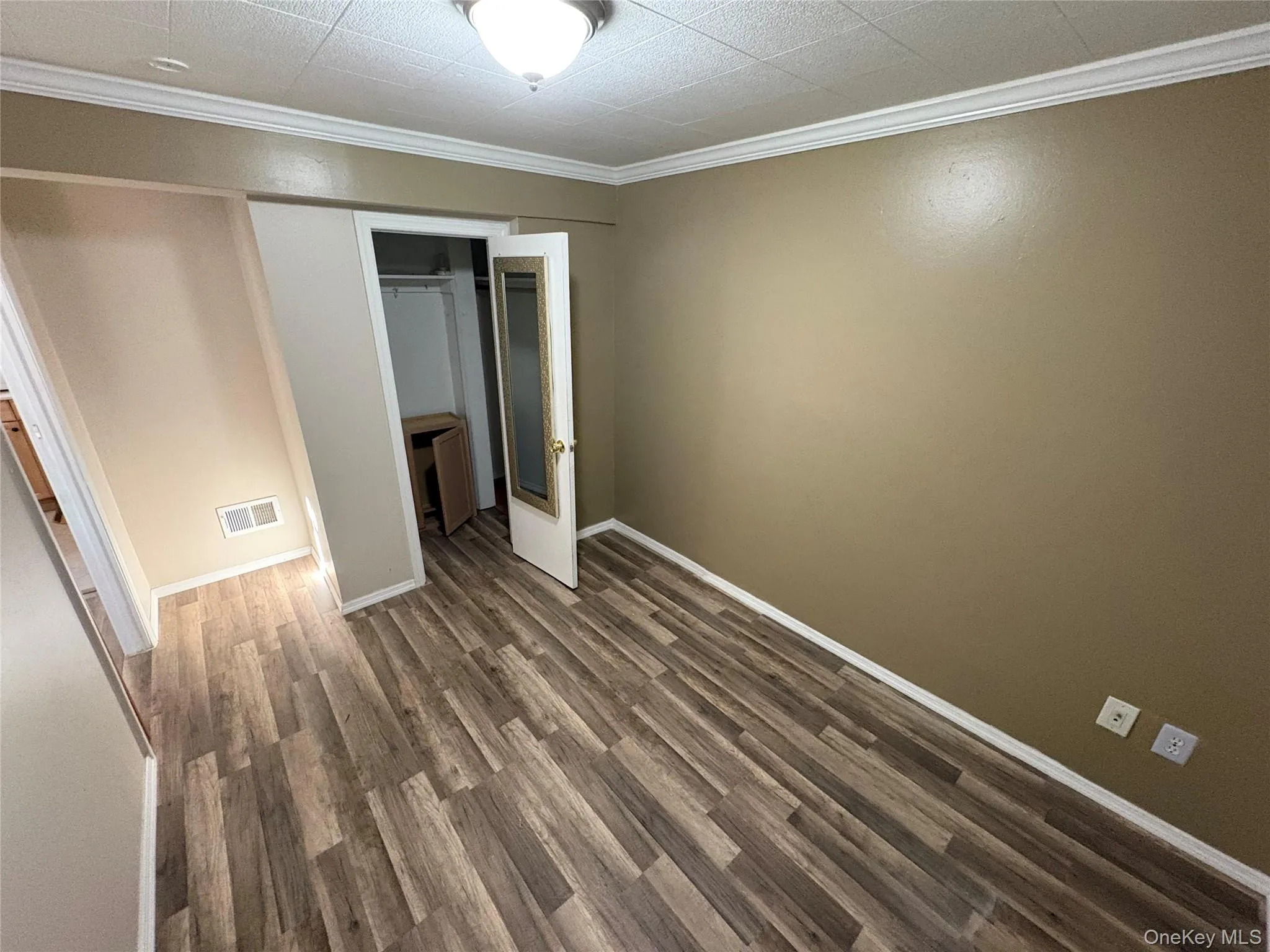 Unfurnished bedroom featuring crown molding, dark wood-style flooring, and a closet Unfurnished bedroom featuring crown molding, dark wood-style flooring, and a closet