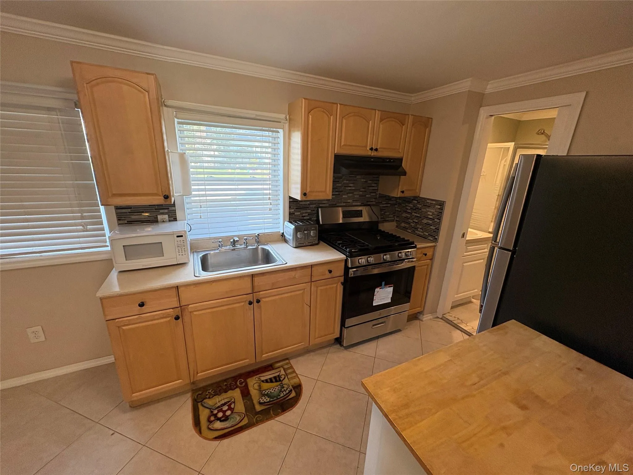 Kitchen with crown molding, light tile patterned flooring, stainless steel appliances, backsplash, and under cabinet range hood Kitchen with crown molding, light tile patterned flooring, stainless steel appliances, backsplash, and under cabinet range hood