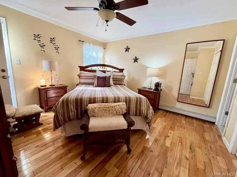 Bedroom with a baseboard heating unit, ornamental molding, light wood-style floors, and ceiling fan Bedroom with a baseboard heating unit, ornamental molding, light wood-style floors, and ceiling fan
