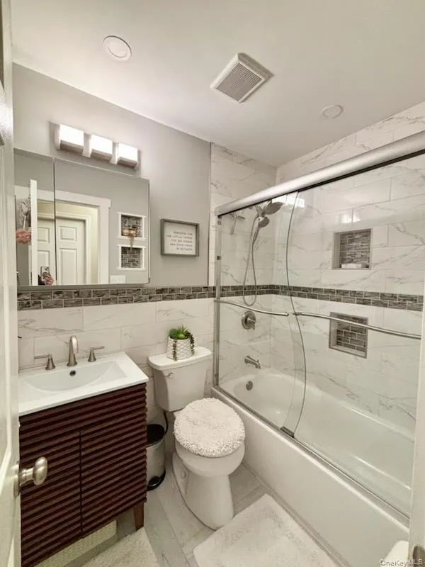 Bathroom featuring tile walls, combined bath / shower with glass door, vanity, and a wainscoted wall Bathroom featuring tile walls, combined bath / shower with glass door, vanity, and a wainscoted wall