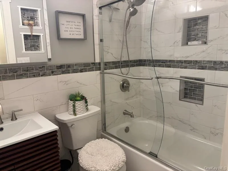 Full bathroom featuring bath / shower combo with glass door, vanity, and tile walls Full bathroom featuring bath / shower combo with glass door, vanity, and tile walls