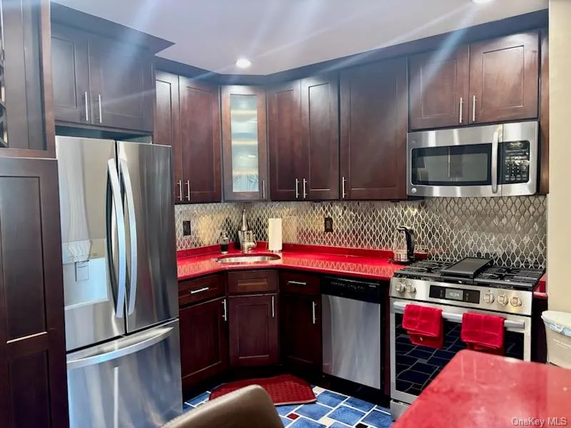 Kitchen featuring stainless steel appliances, backsplash, glass insert cabinets, recessed lighting, and dark brown cabinets Kitchen featuring stainless steel appliances, backsplash, glass insert cabinets, recessed lighting, and dark brown cabinets
