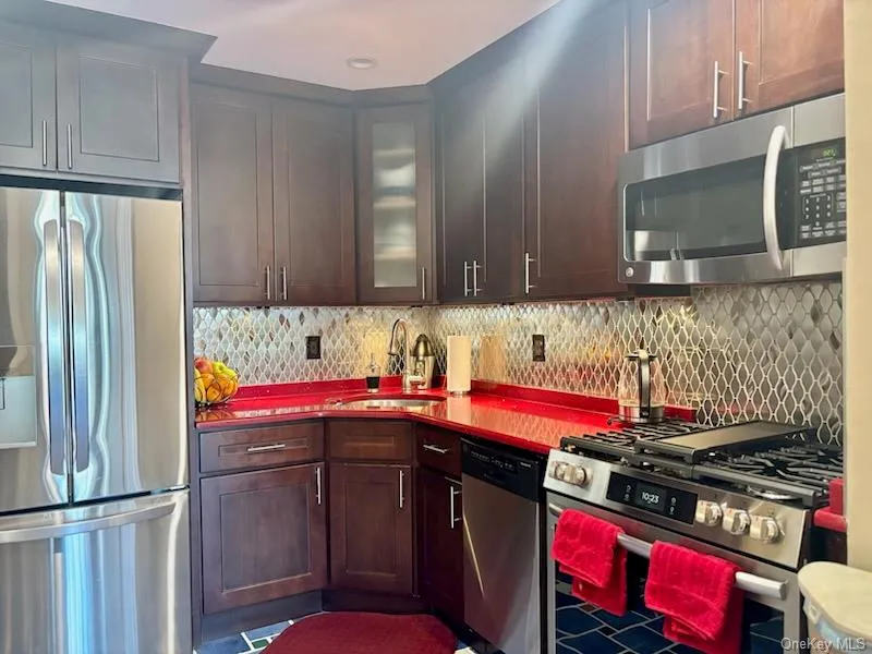 Kitchen featuring appliances with stainless steel finishes, glass insert cabinets, tasteful backsplash, and dark brown cabinets Kitchen featuring appliances with stainless steel finishes, glass insert cabinets, tasteful backsplash, and dark brown cabinets