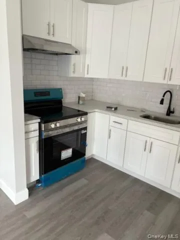 Kitchen with electric range, white cabinets, backsplash, under cabinet range hood, and dark wood-type flooring Kitchen with electric range, white cabinets, backsplash, under cabinet range hood, and dark wood-type flooring