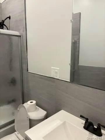 Bathroom featuring vanity, combined bath / shower with glass door, and tile walls Bathroom featuring vanity, combined bath / shower with glass door, and tile walls