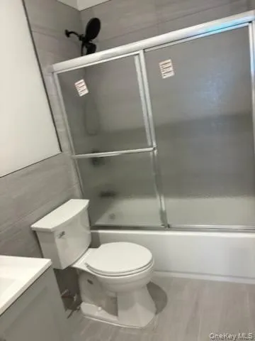 Full bath featuring combined bath / shower with glass door, vanity, light wood-style floors, and tile walls Full bath featuring combined bath / shower with glass door, vanity, light wood-style floors, and tile walls