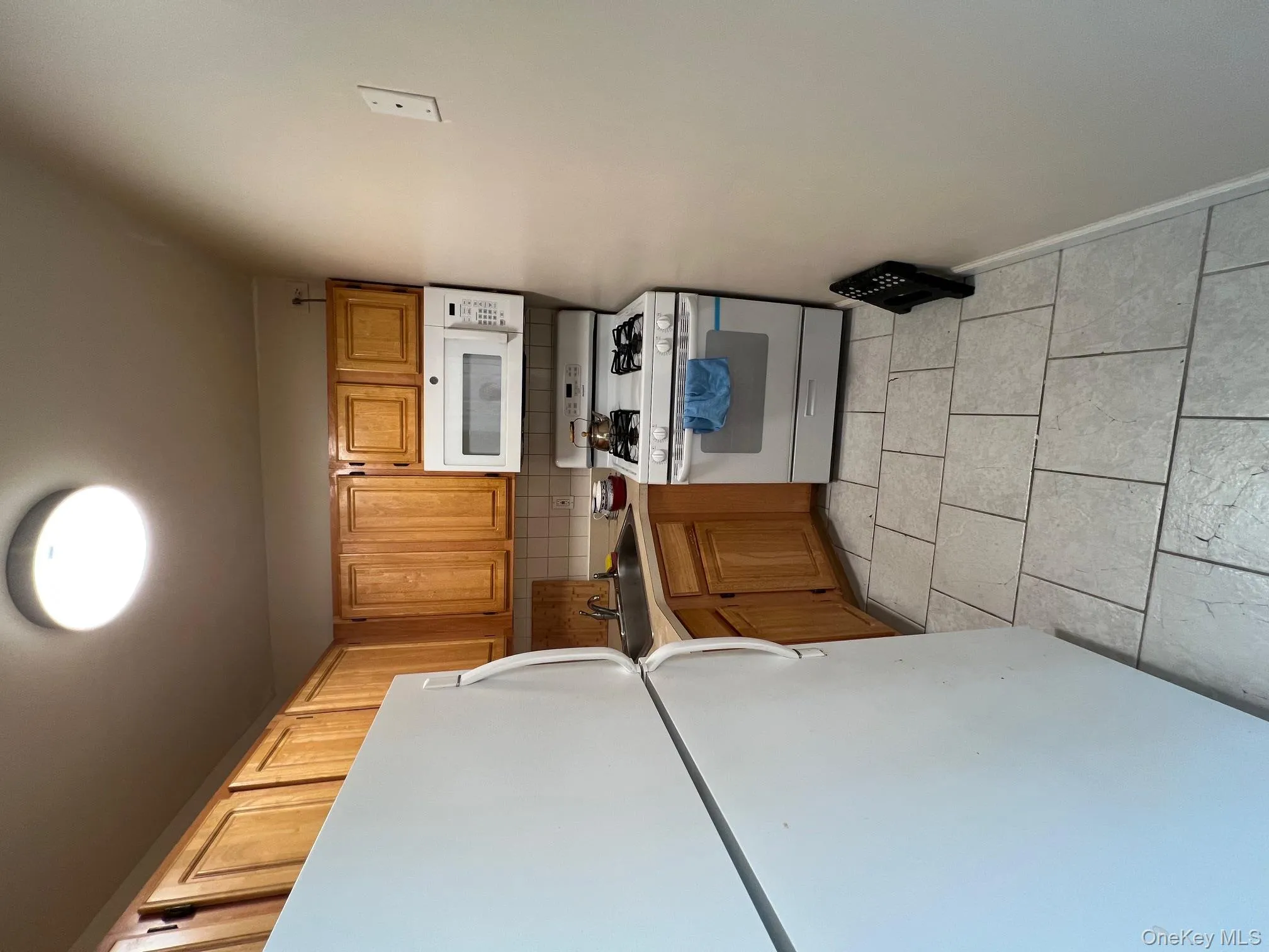 Kitchen featuring white appliances, light countertops, backsplash, light tile patterned floors, and brown cabinets Kitchen featuring white appliances, light countertops, backsplash, light tile patterned floors, and brown cabinets