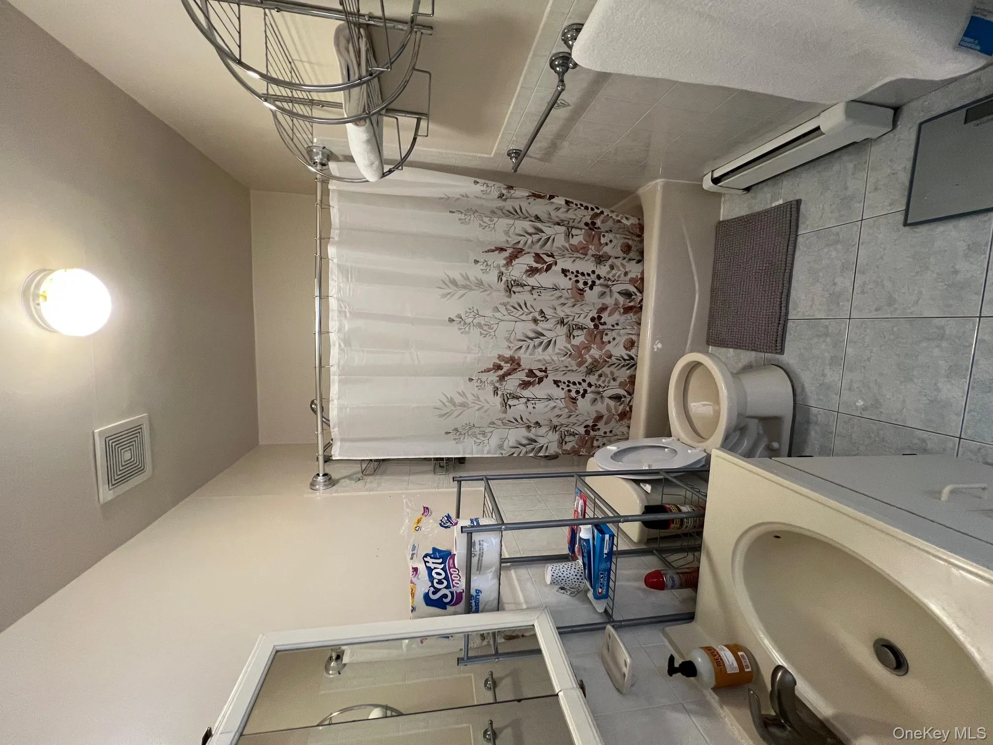 Bathroom featuring tile walls, a baseboard heating unit, shower / tub combo with curtain, vanity, and light tile patterned floors Bathroom featuring tile walls, a baseboard heating unit, shower / tub combo with curtain, vanity, and light tile patterned floors