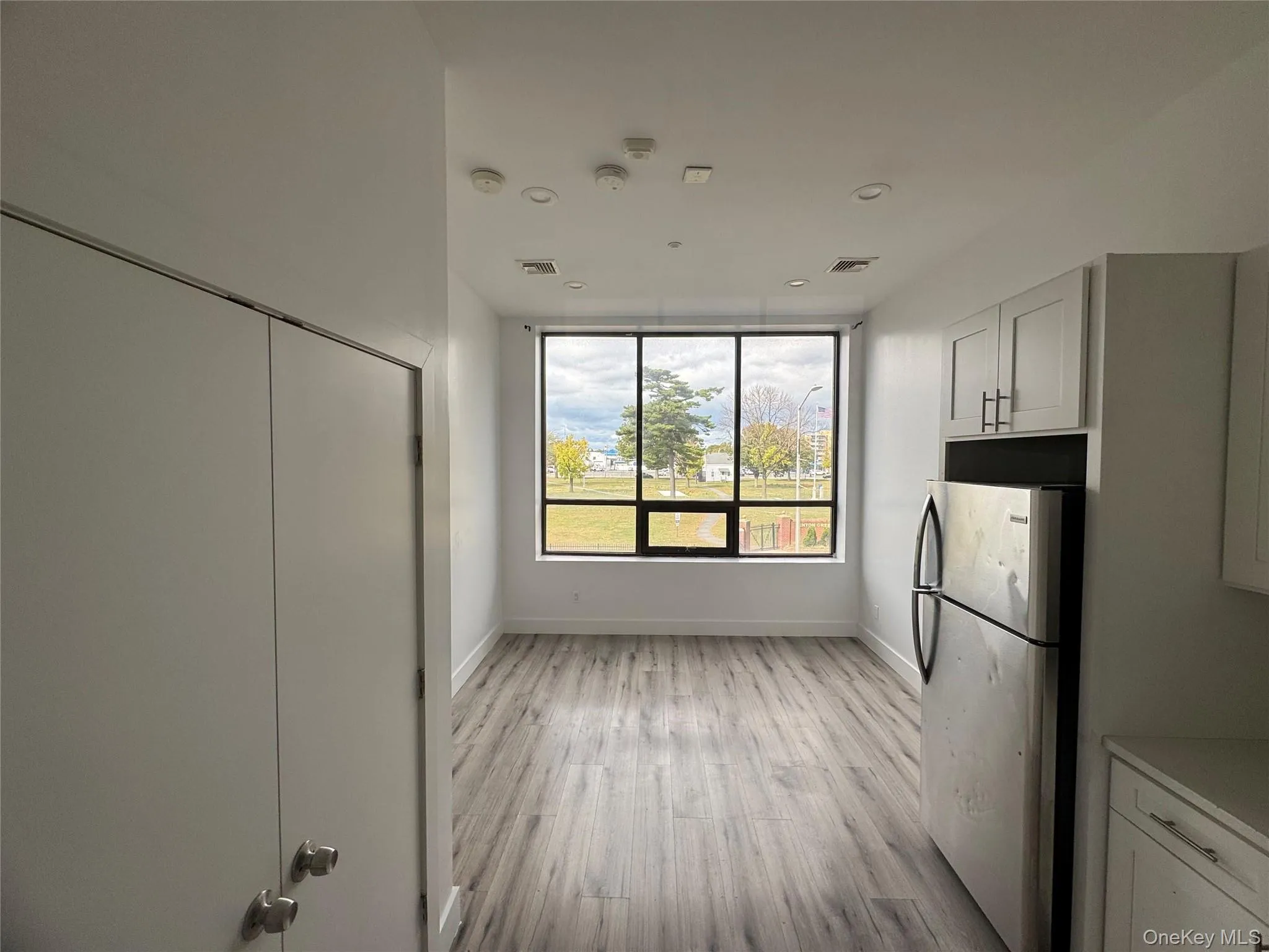 Kitchen featuring freestanding refrigerator, white cabinetry, light wood-type flooring, and light countertops Kitchen featuring freestanding refrigerator, white cabinetry, light wood-type flooring, and light countertops