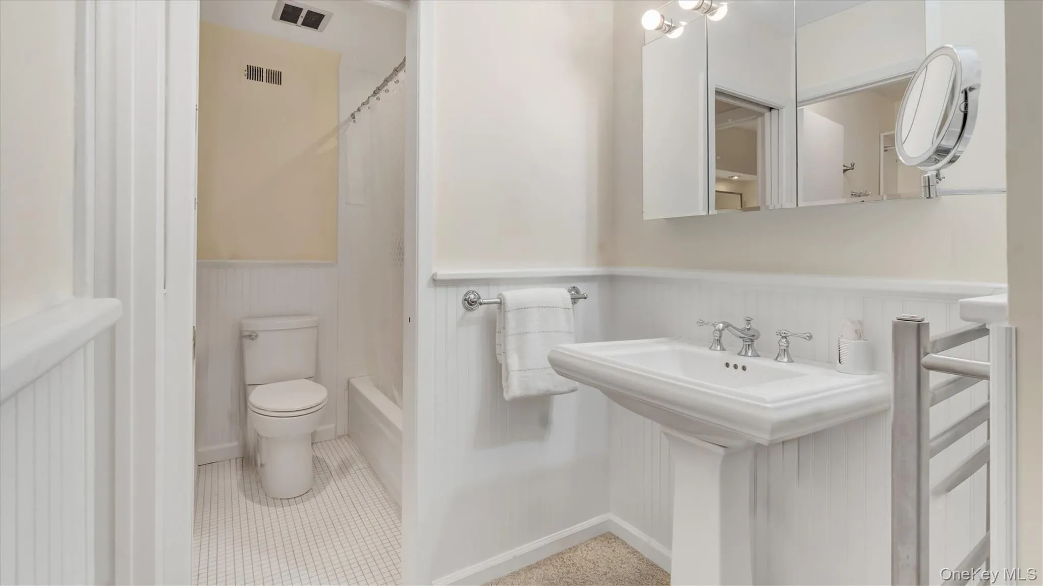 Primary Bathroom featuring light tile patterned flooring, shower / bath combination with curtain, and a wainscoted wall Primary Bathroom featuring light tile patterned flooring, shower / bath combination with curtain, and a wainscoted wall