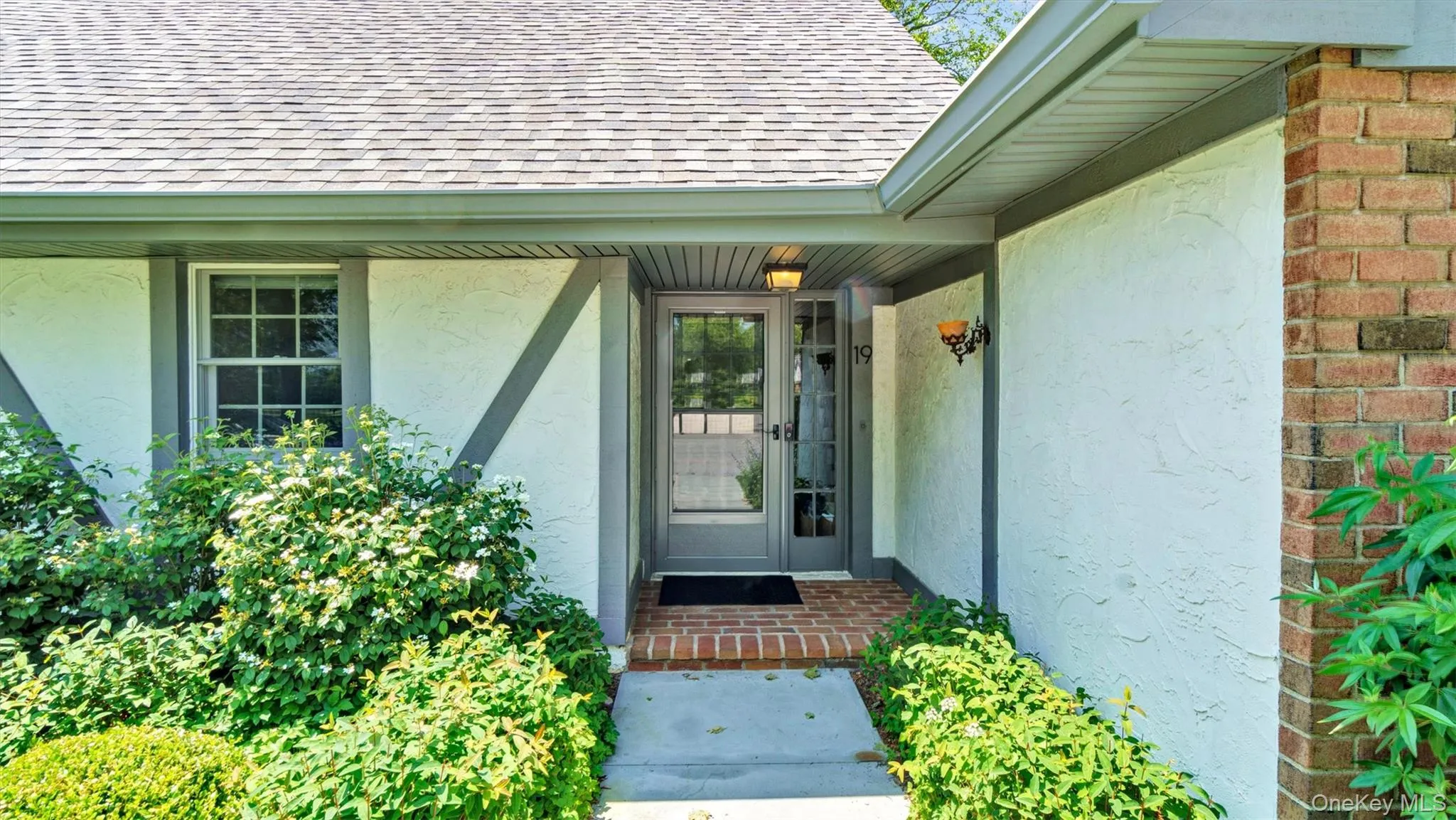 Entrance to property with a shingled roof, stucco siding, and brick siding Entrance to property with a shingled roof, stucco siding, and brick siding
