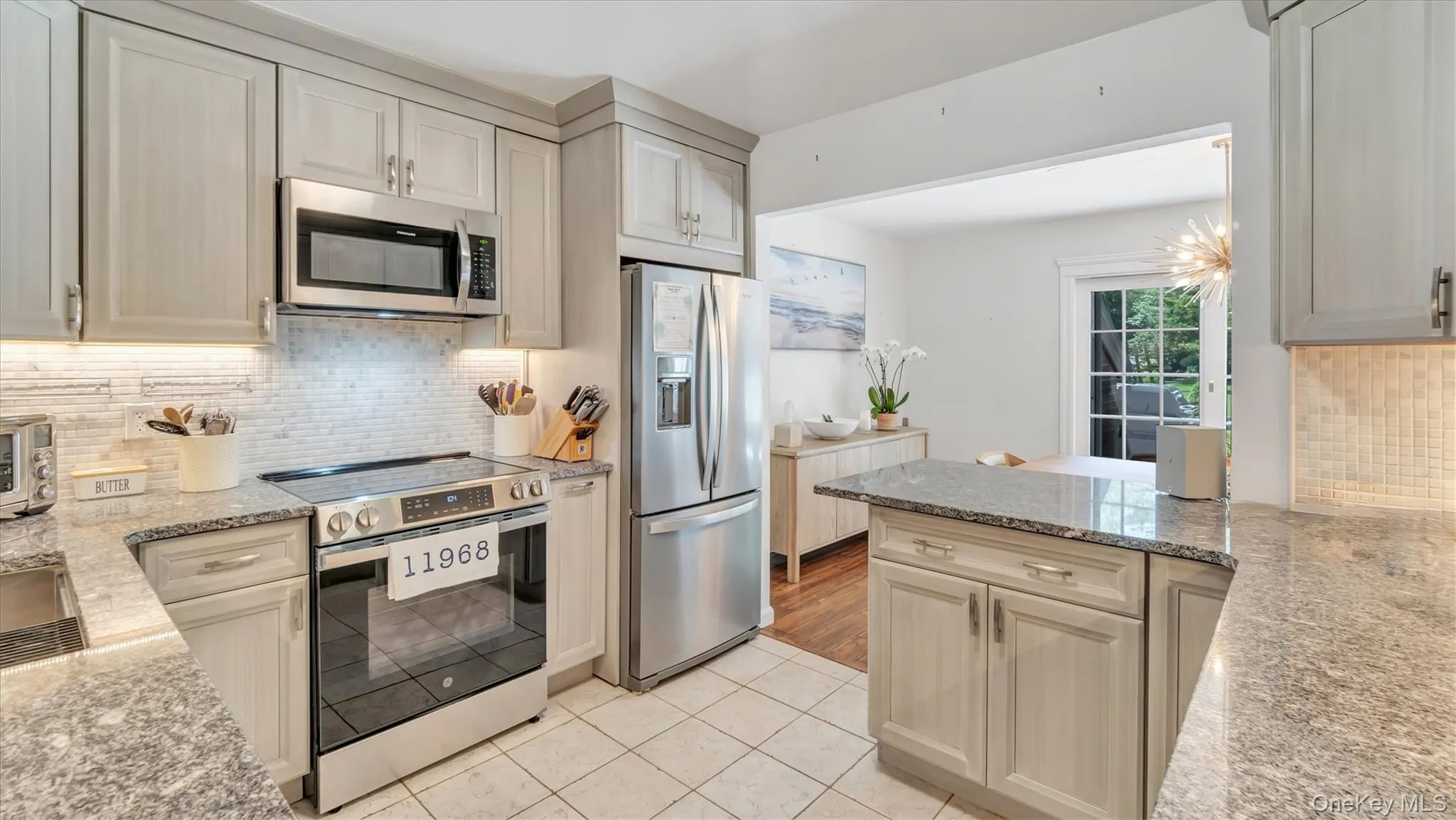Kitchen with tasteful backsplash, light stone counters, appliances with stainless steel finishes, light tile patterned floors, and a peninsula Kitchen with tasteful backsplash, light stone counters, appliances with stainless steel finishes, light tile patterned floors, and a peninsula