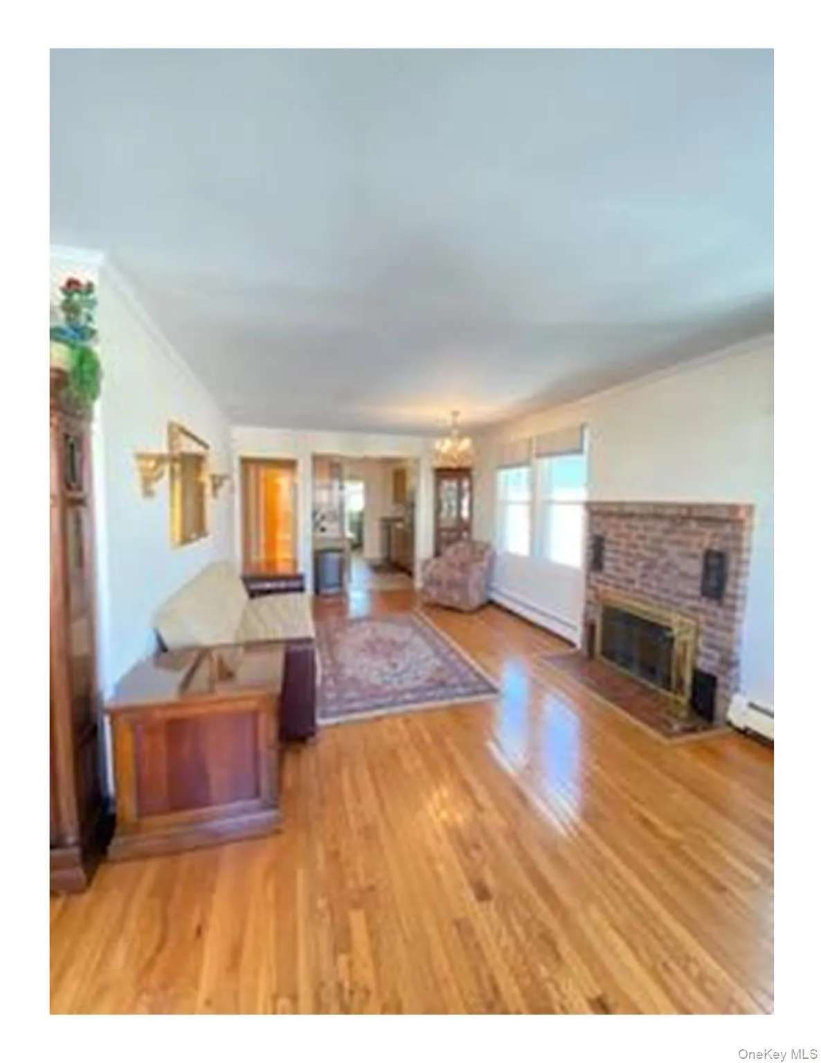 Living area with crown molding, a chandelier, a brick fireplace, light wood-style floors, and baseboard heating Living area with crown molding, a chandelier, a brick fireplace, light wood-style floors, and baseboard heating