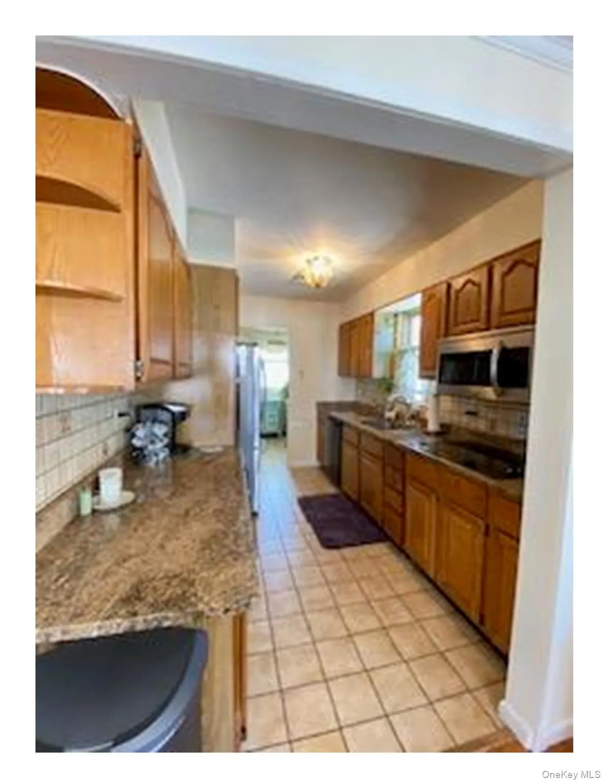 Kitchen featuring decorative backsplash, brown cabinetry, light tile patterned floors, appliances with stainless steel finishes, and open shelves Kitchen featuring decorative backsplash, brown cabinetry, light tile patterned floors, appliances with stainless steel finishes, and open shelves
