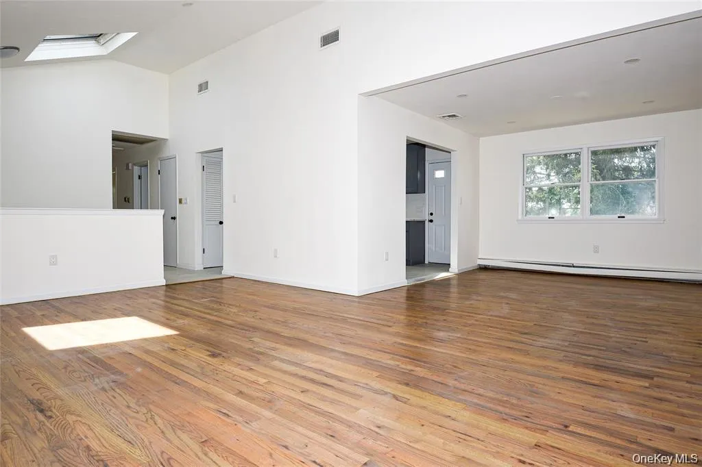 Unfurnished living room featuring light wood-style flooring, a baseboard heating unit, and vaulted ceiling Unfurnished living room featuring light wood-style flooring, a baseboard heating unit, and vaulted ceiling