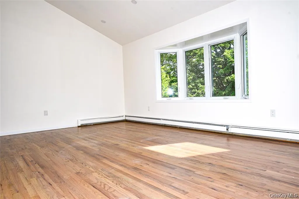 Empty room featuring light wood-type flooring, a baseboard heating unit, and vaulted ceiling Empty room featuring light wood-type flooring, a baseboard heating unit, and vaulted ceiling