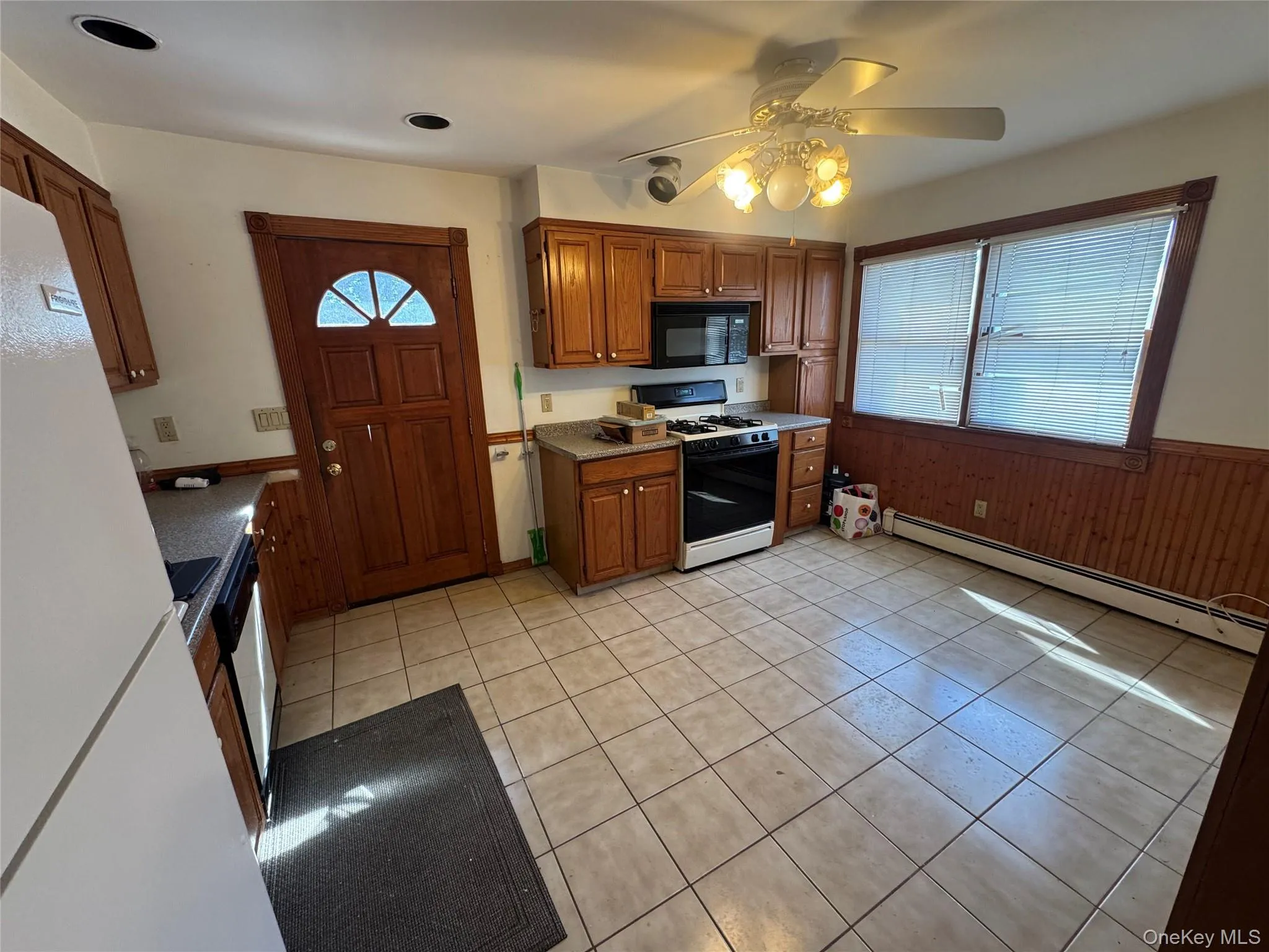 Kitchen with baseboard heating, gas range oven, light tile patterned floors, brown cabinets, and wainscoting Kitchen with baseboard heating, gas range oven, light tile patterned floors, brown cabinets, and wainscoting