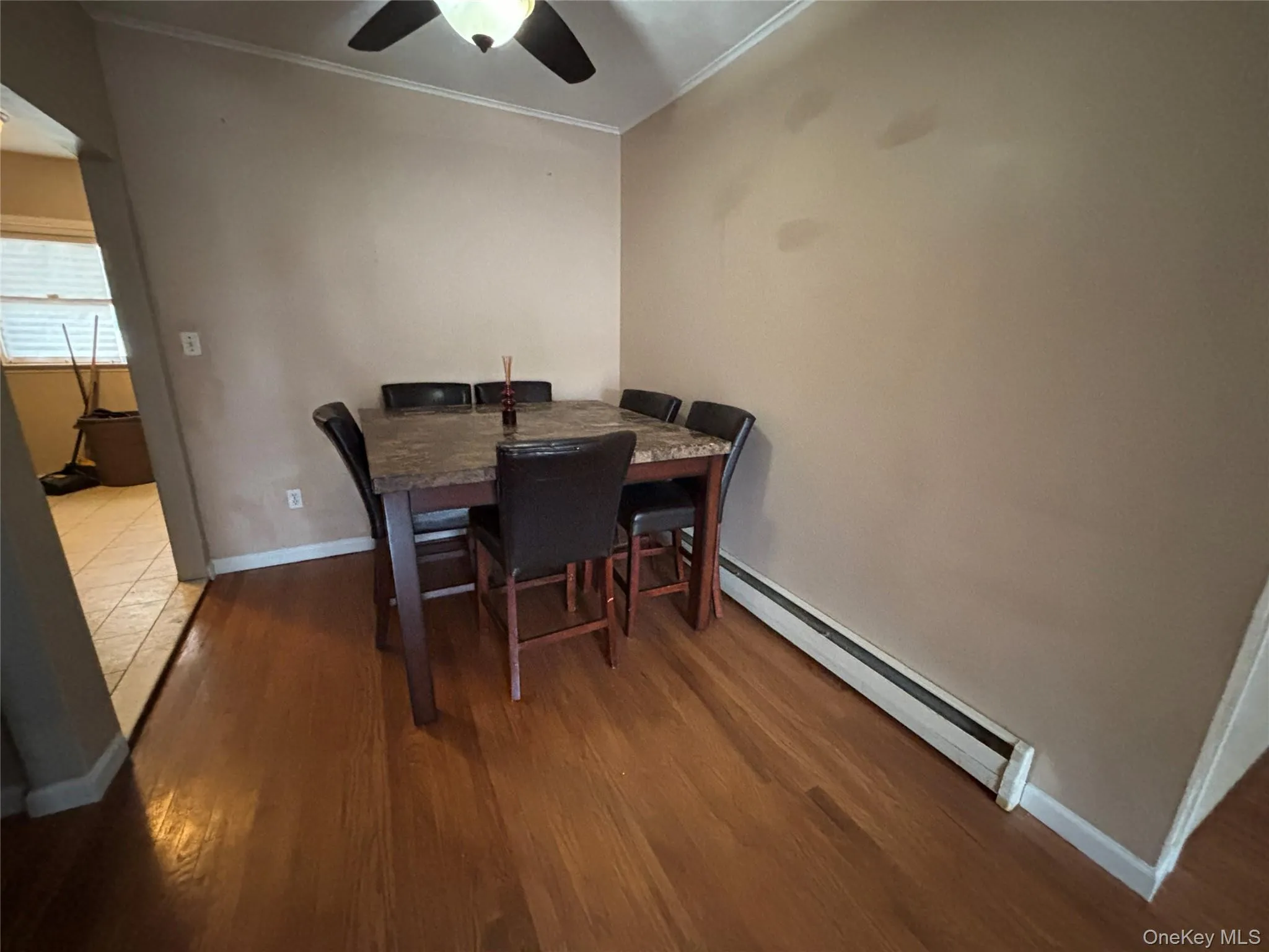 Dining space with ornamental molding, dark wood-style flooring, baseboard heating, and a ceiling fan Dining space with ornamental molding, dark wood-style flooring, baseboard heating, and a ceiling fan