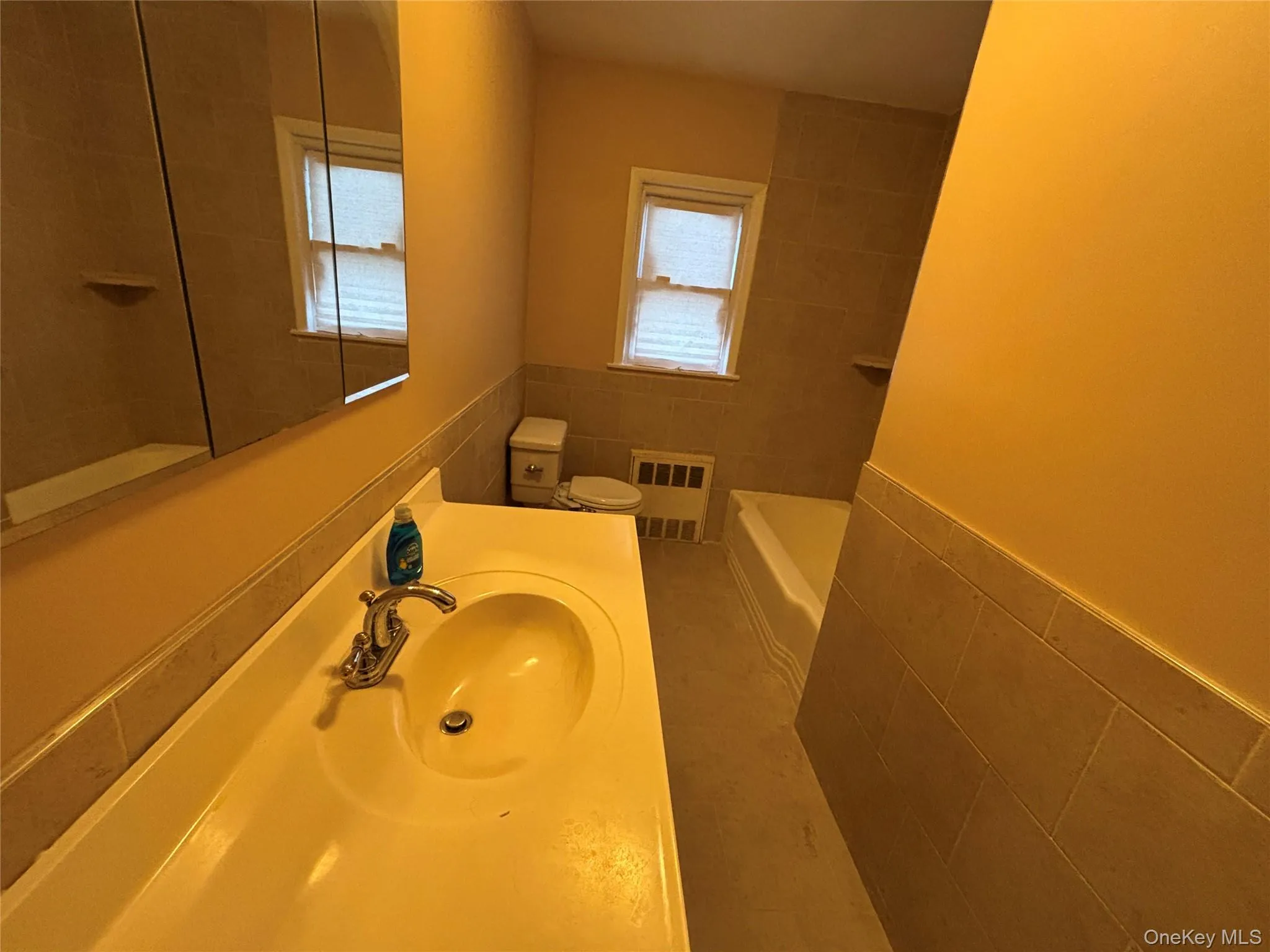 Full bath with tile walls, vanity, radiator, light tile patterned floors, and a wainscoted wall Full bath with tile walls, vanity, radiator, light tile patterned floors, and a wainscoted wall