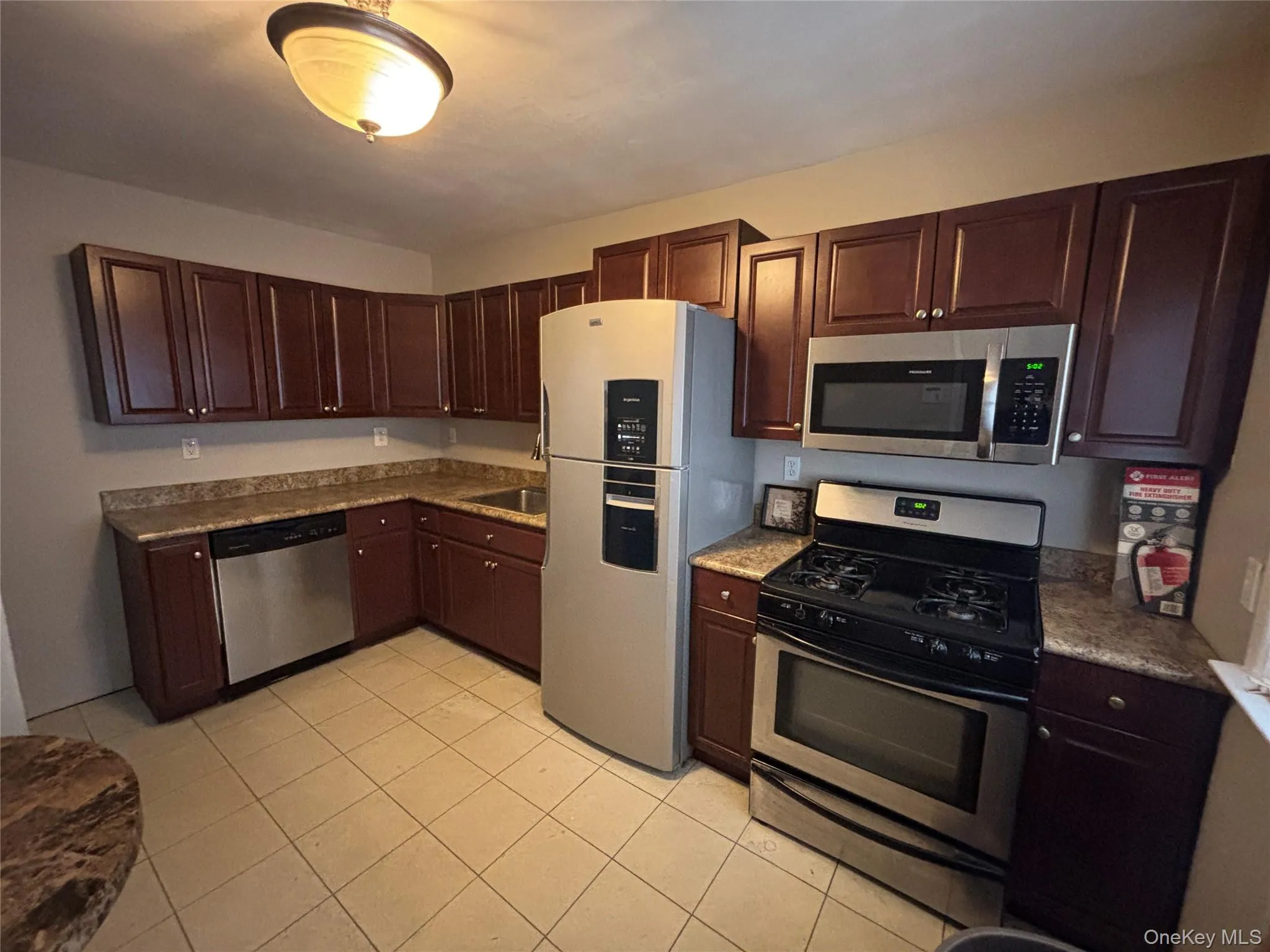 Kitchen with stainless steel appliances, dark brown cabinets, light tile patterned floors, and light stone counters Kitchen with stainless steel appliances, dark brown cabinets, light tile patterned floors, and light stone counters