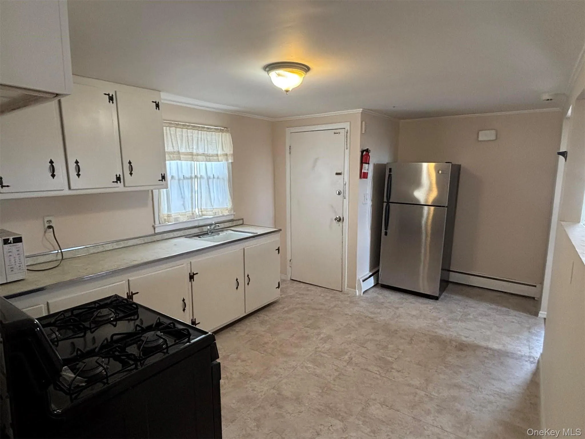 Kitchen featuring black gas range oven, light countertops, freestanding refrigerator, white cabinetry, and crown molding Kitchen featuring black gas range oven, light countertops, freestanding refrigerator, white cabinetry, and crown molding