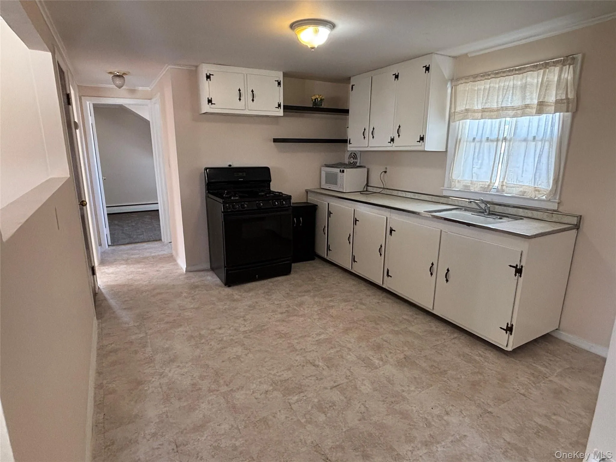 Kitchen featuring gas stove, light countertops, open shelves, white cabinets, and white microwave Kitchen featuring gas stove, light countertops, open shelves, white cabinets, and white microwave