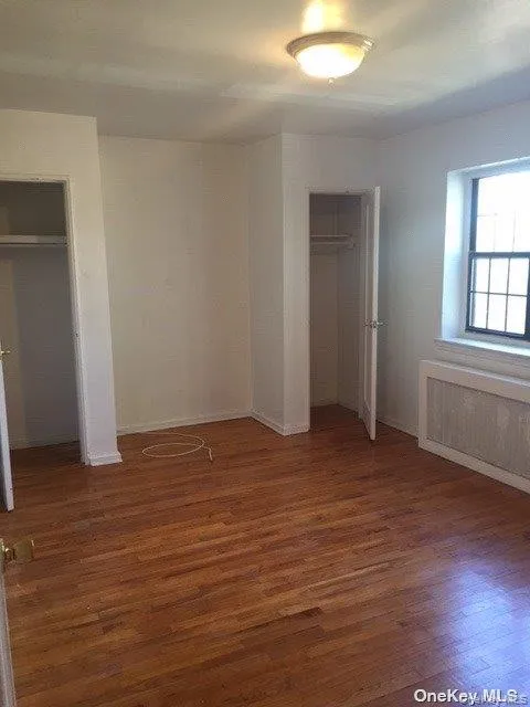 Unfurnished bedroom featuring radiator heating unit, dark wood-style flooring, and two closets Unfurnished bedroom featuring radiator heating unit, dark wood-style flooring, and two closets