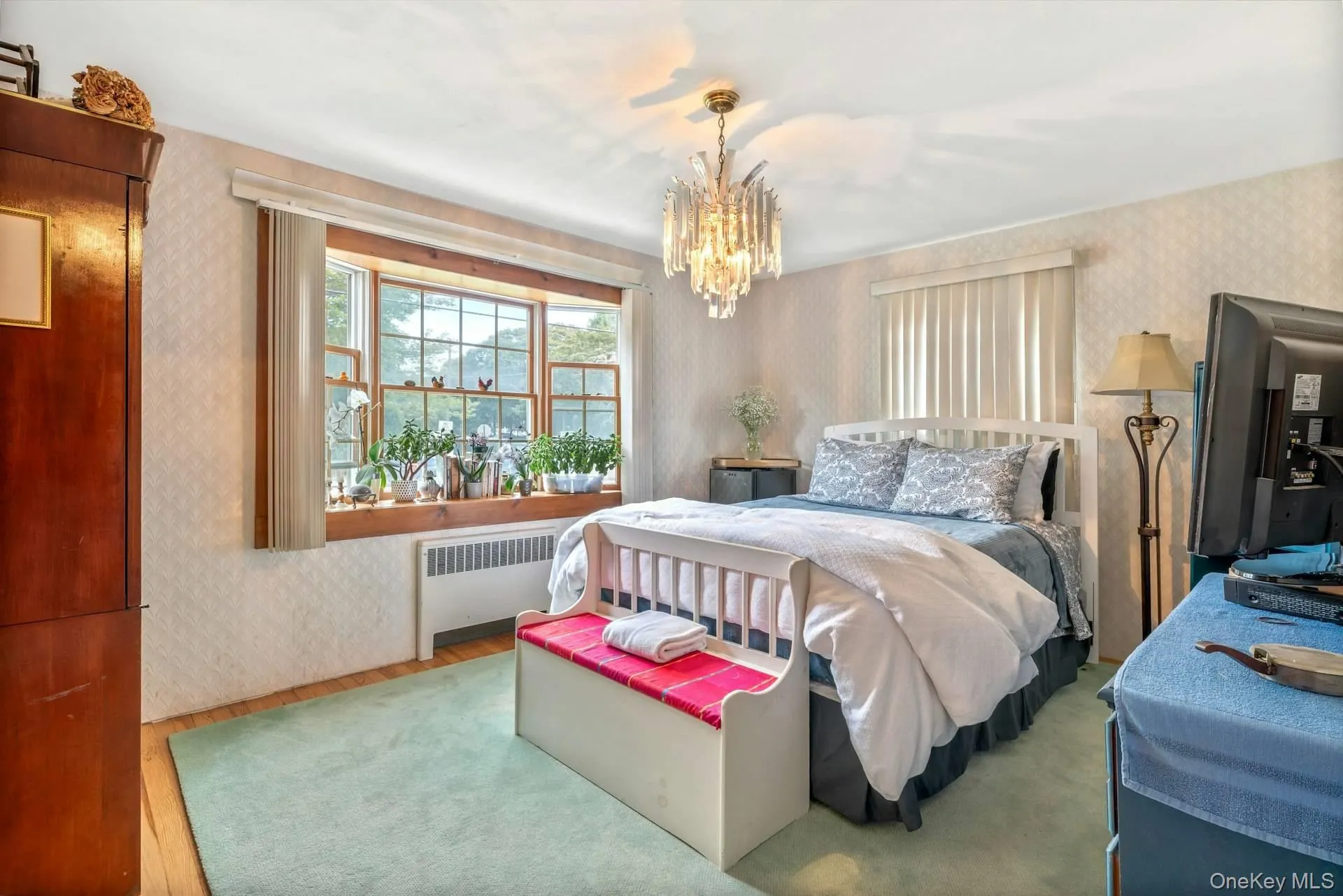 Bedroom featuring wallpapered walls, wood finished floors, radiator, and a chandelier Bedroom featuring wallpapered walls, wood finished floors, radiator, and a chandelier