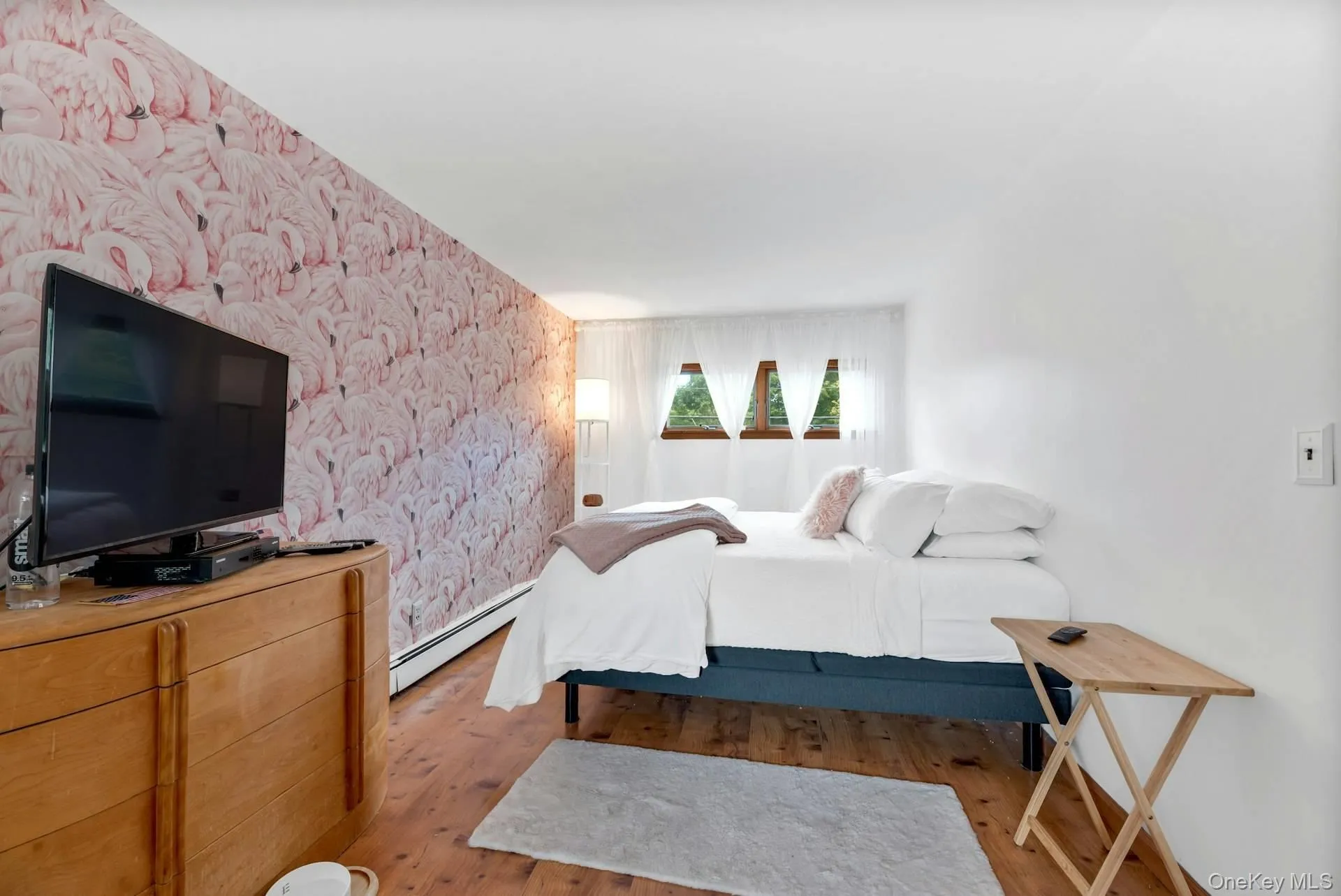 Bedroom with wood finished floors, a baseboard radiator, and wallpapered walls Bedroom with wood finished floors, a baseboard radiator, and wallpapered walls