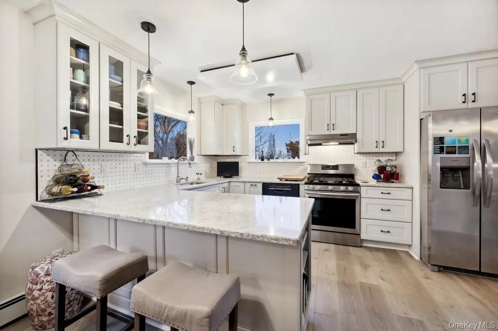 Kitchen featuring stainless steel appliances, light stone countertops, a peninsula, and white cabinetry Kitchen featuring stainless steel appliances, light stone countertops, a peninsula, and white cabinetry