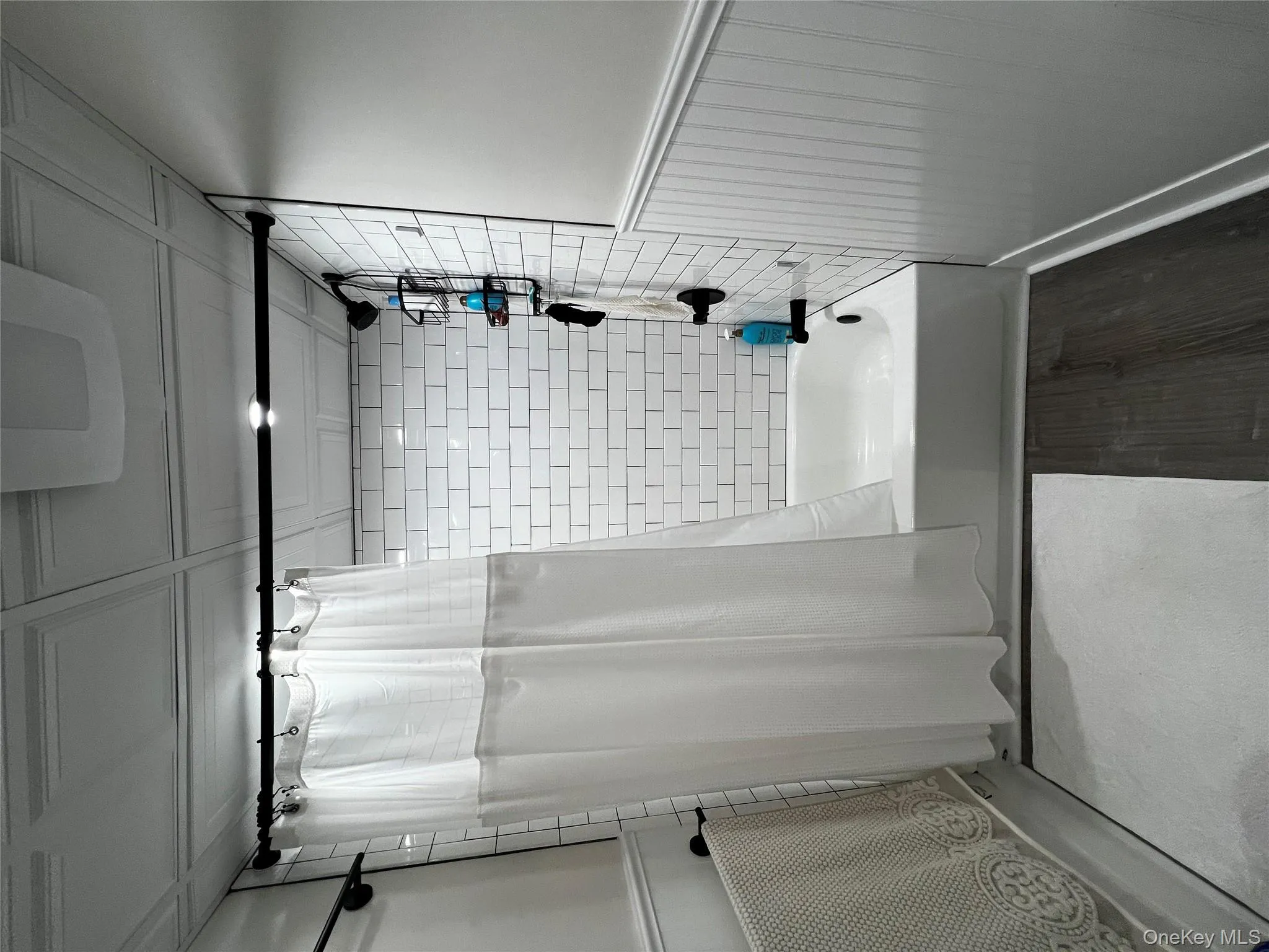 Bathroom featuring shower / tub combo, dark wood-type flooring, and wainscoting Bathroom featuring shower / tub combo, dark wood-type flooring, and wainscoting