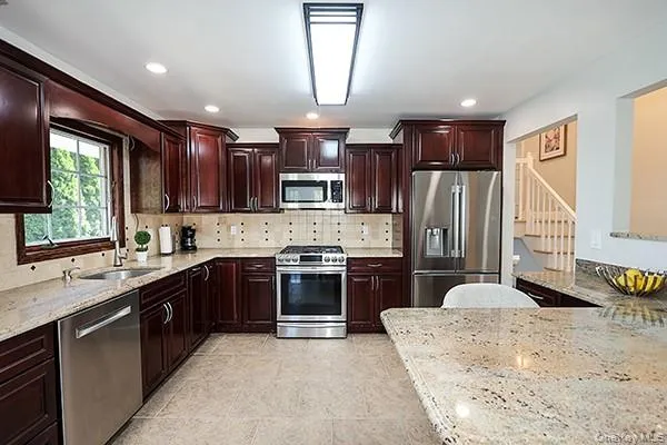 Kitchen featuring stainless steel appliances, light stone counters, dark brown cabinets, tasteful backsplash, and recessed lighting Kitchen featuring stainless steel appliances, light stone counters, dark brown cabinets, tasteful backsplash, and recessed lighting