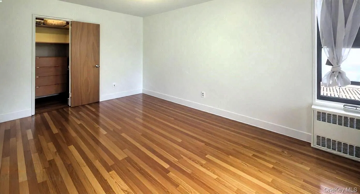 Unfurnished bedroom with radiator, dark wood finished floors, and a spacious closet Unfurnished bedroom with radiator, dark wood finished floors, and a spacious closet