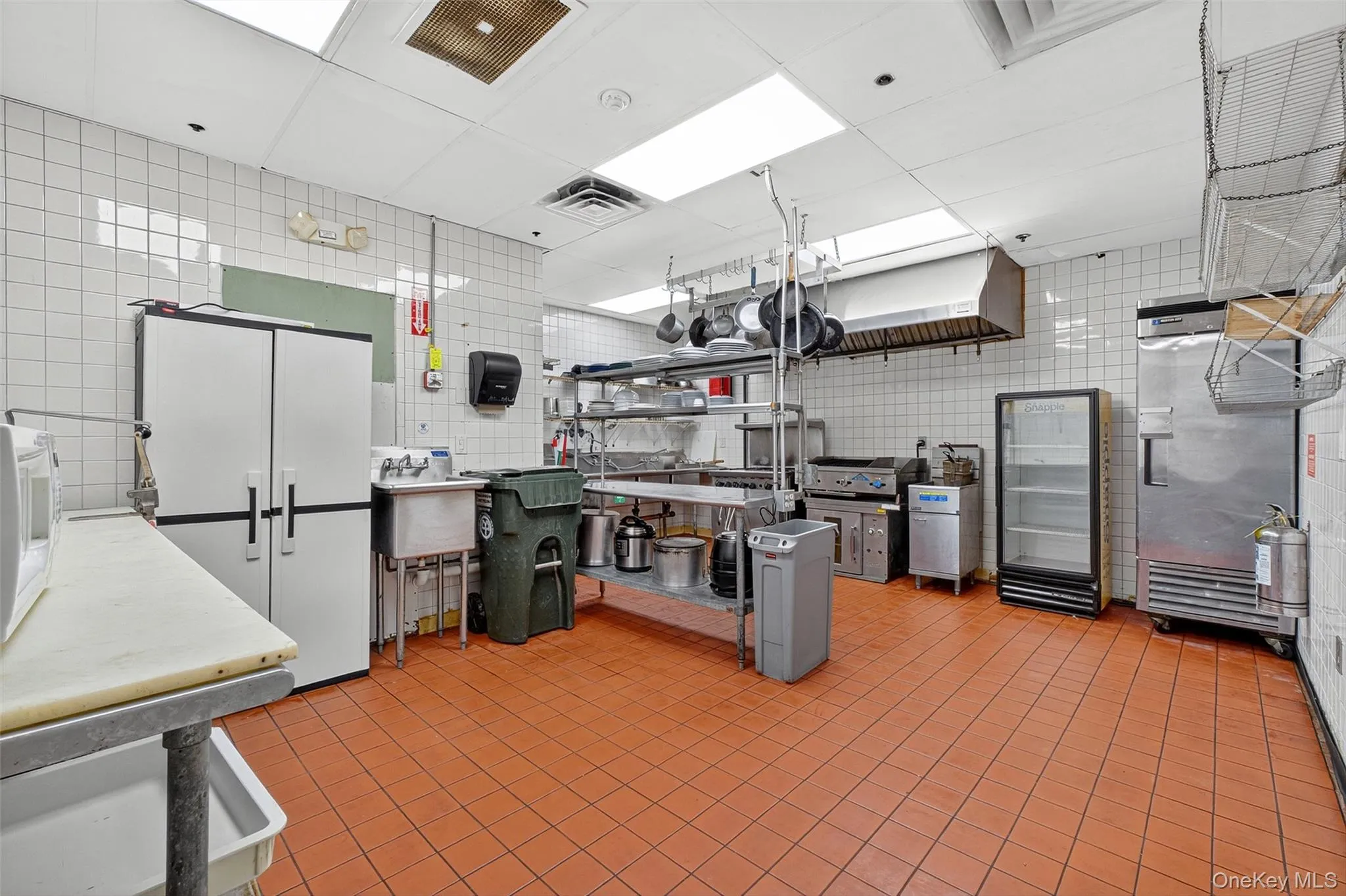 Kitchen featuring tile walls, light countertops, white microwave, and stainless steel fridge Kitchen featuring tile walls, light countertops, white microwave, and stainless steel fridge