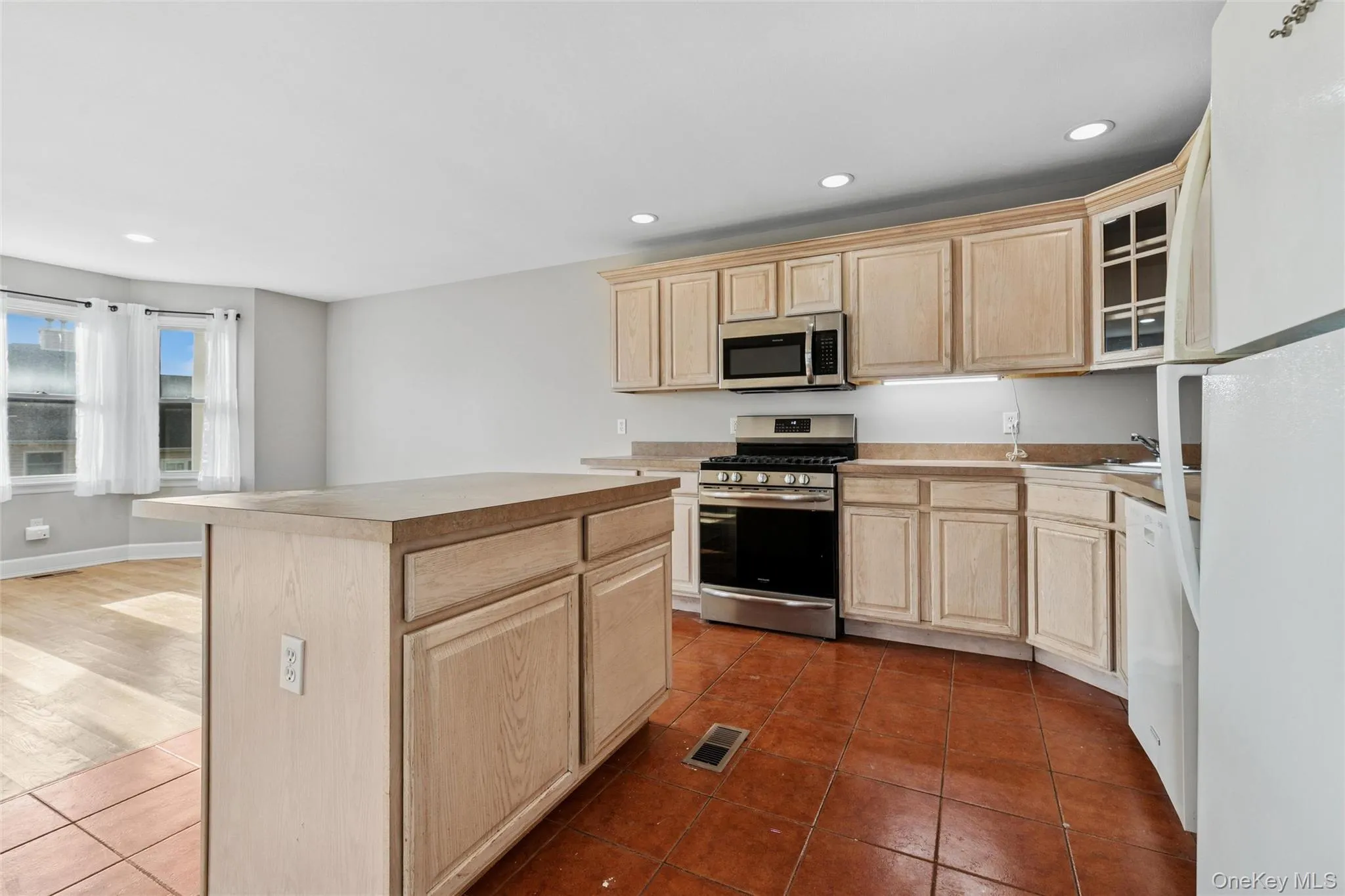 Kitchen featuring light brown cabinetry, stainless steel appliances, recessed lighting, a kitchen island, and glass insert cabinets Kitchen featuring light brown cabinetry, stainless steel appliances, recessed lighting, a kitchen island, and glass insert cabinets