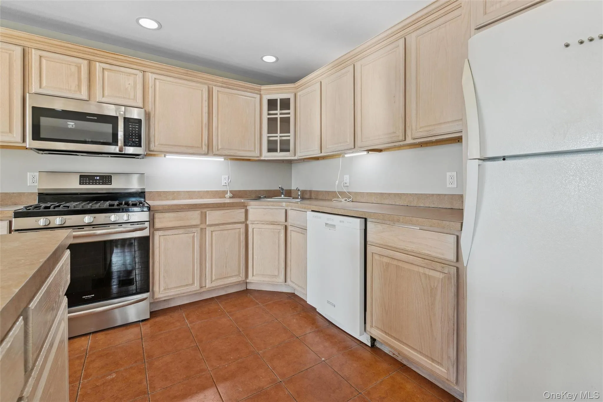 Kitchen featuring appliances with stainless steel finishes, light brown cabinetry, glass insert cabinets, light tile patterned flooring, and recessed lighting Kitchen featuring appliances with stainless steel finishes, light brown cabinetry, glass insert cabinets, light tile patterned flooring, and recessed lighting