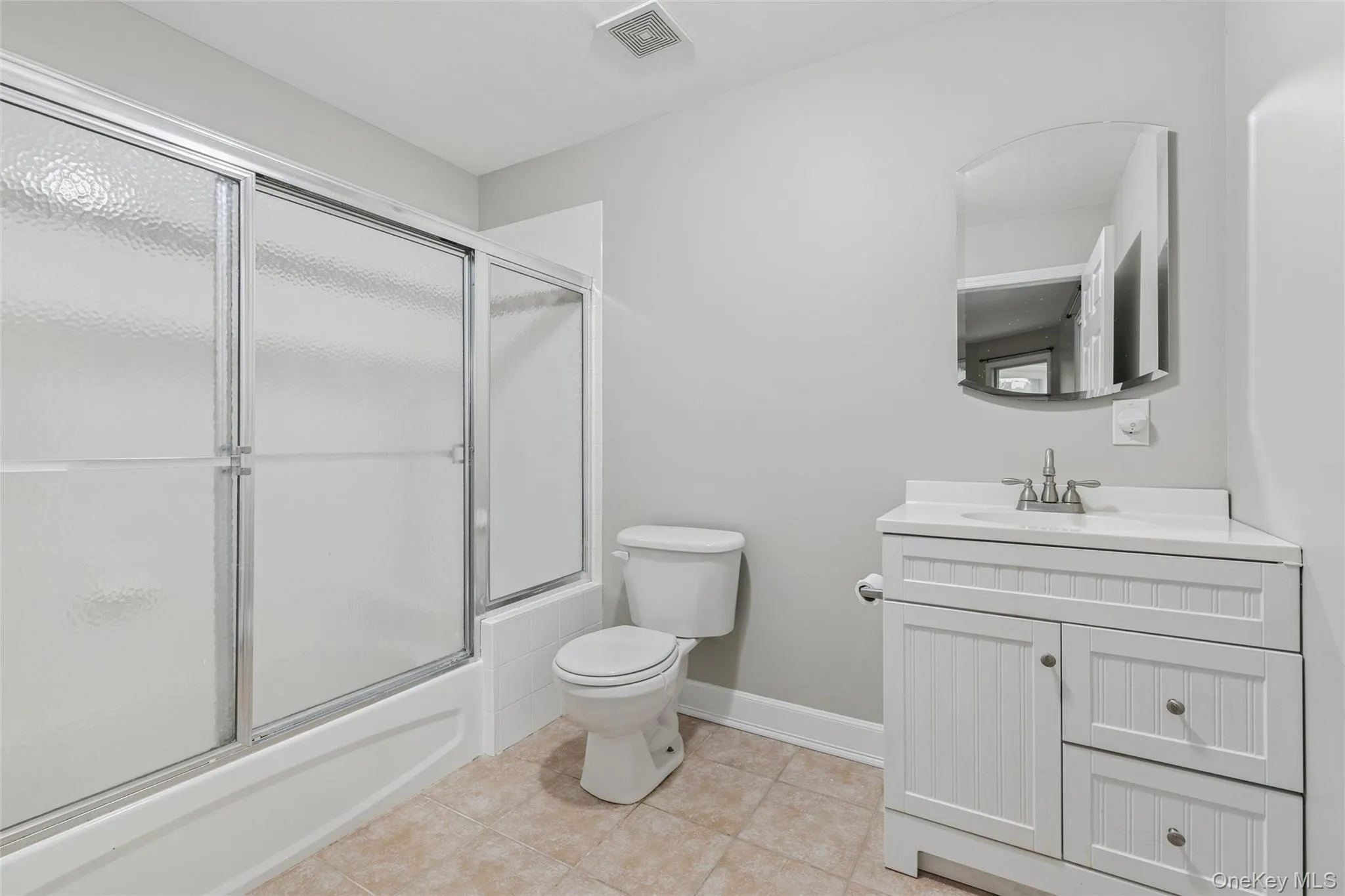 Bathroom with vanity, shower / bath combination with glass door, and light tile patterned flooring Bathroom with vanity, shower / bath combination with glass door, and light tile patterned flooring