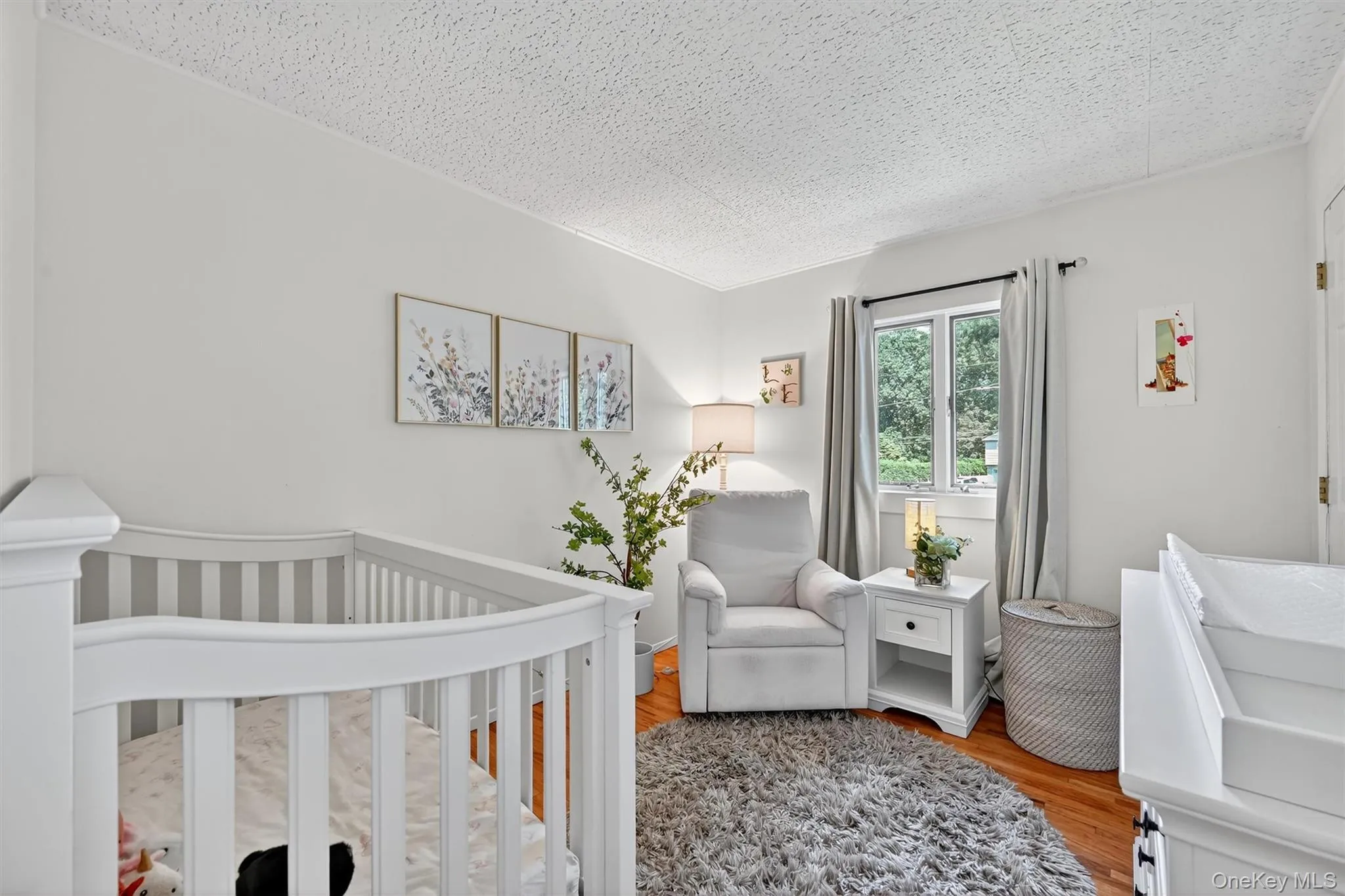 Bedroom featuring wood finished floors, a crib, and a textured ceiling Bedroom featuring wood finished floors, a crib, and a textured ceiling