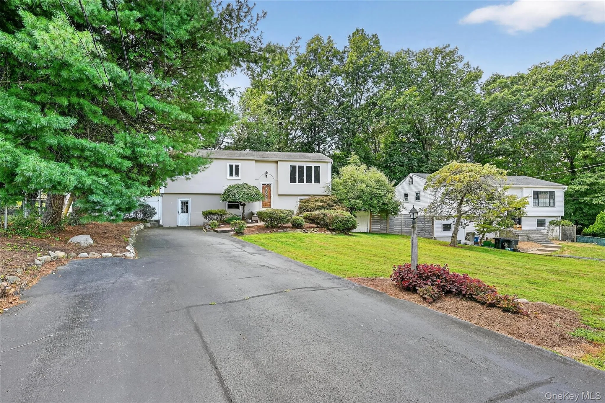 Bi-level home featuring a front lawn, asphalt driveway, view of wooded area, and stucco siding Bi-level home featuring a front lawn, asphalt driveway, view of wooded area, and stucco siding