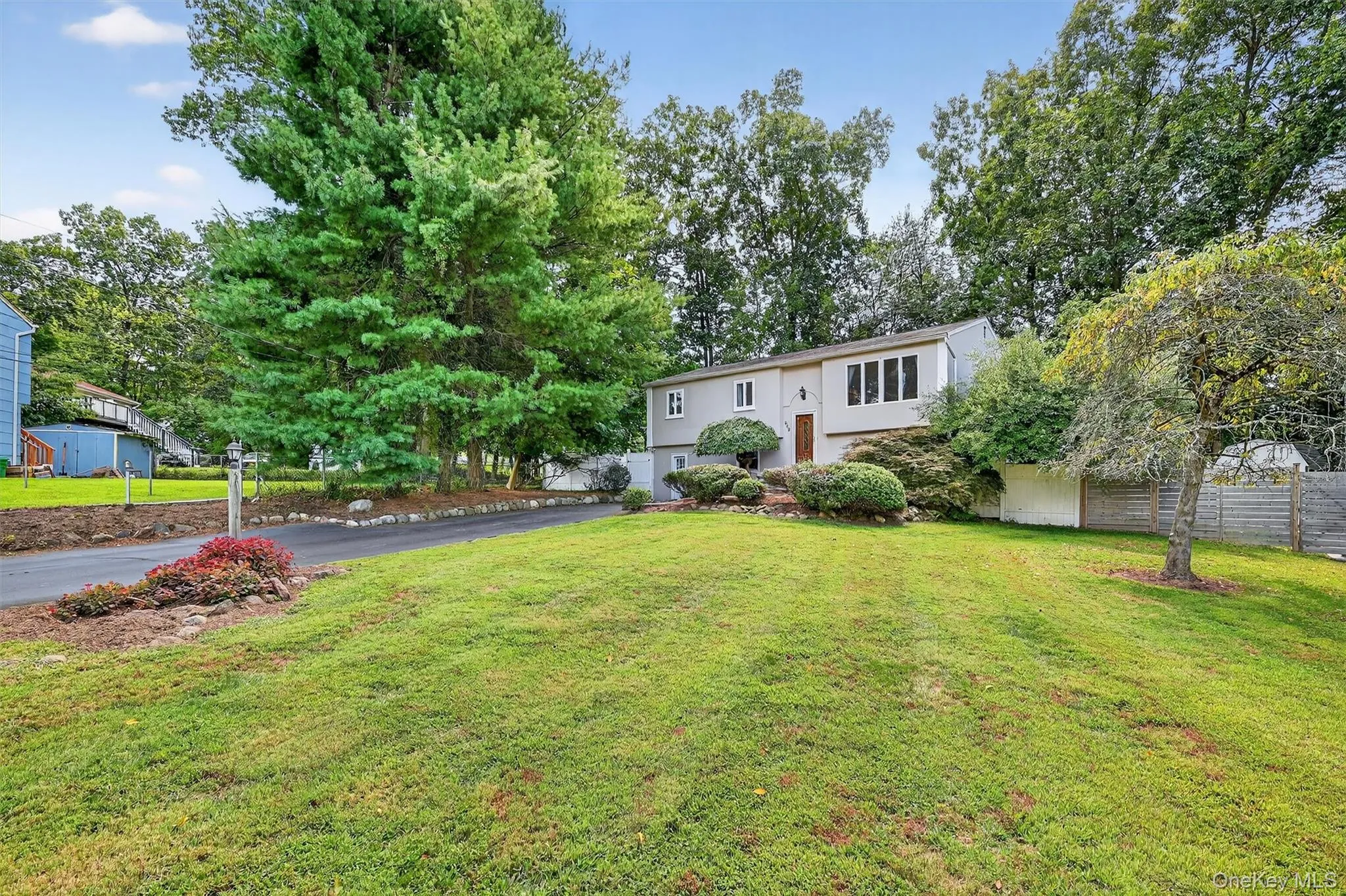 Split foyer home with a garage, driveway, view of wooded area, and stucco siding Split foyer home with a garage, driveway, view of wooded area, and stucco siding