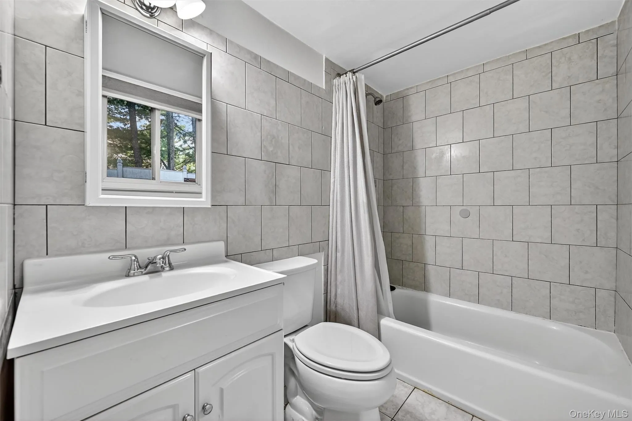 Full bath featuring shower / bath combo, vanity, tile walls, and tile patterned floors Full bath featuring shower / bath combo, vanity, tile walls, and tile patterned floors