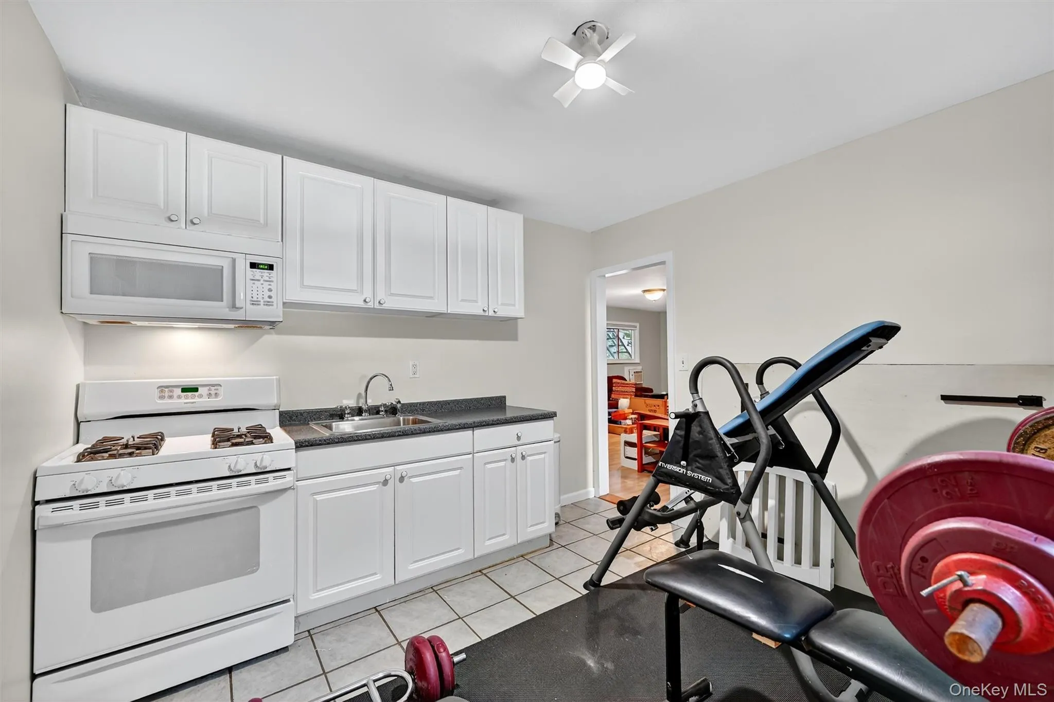 Kitchen featuring white appliances, dark countertops, white cabinetry, and light tile patterned flooring Kitchen featuring white appliances, dark countertops, white cabinetry, and light tile patterned flooring