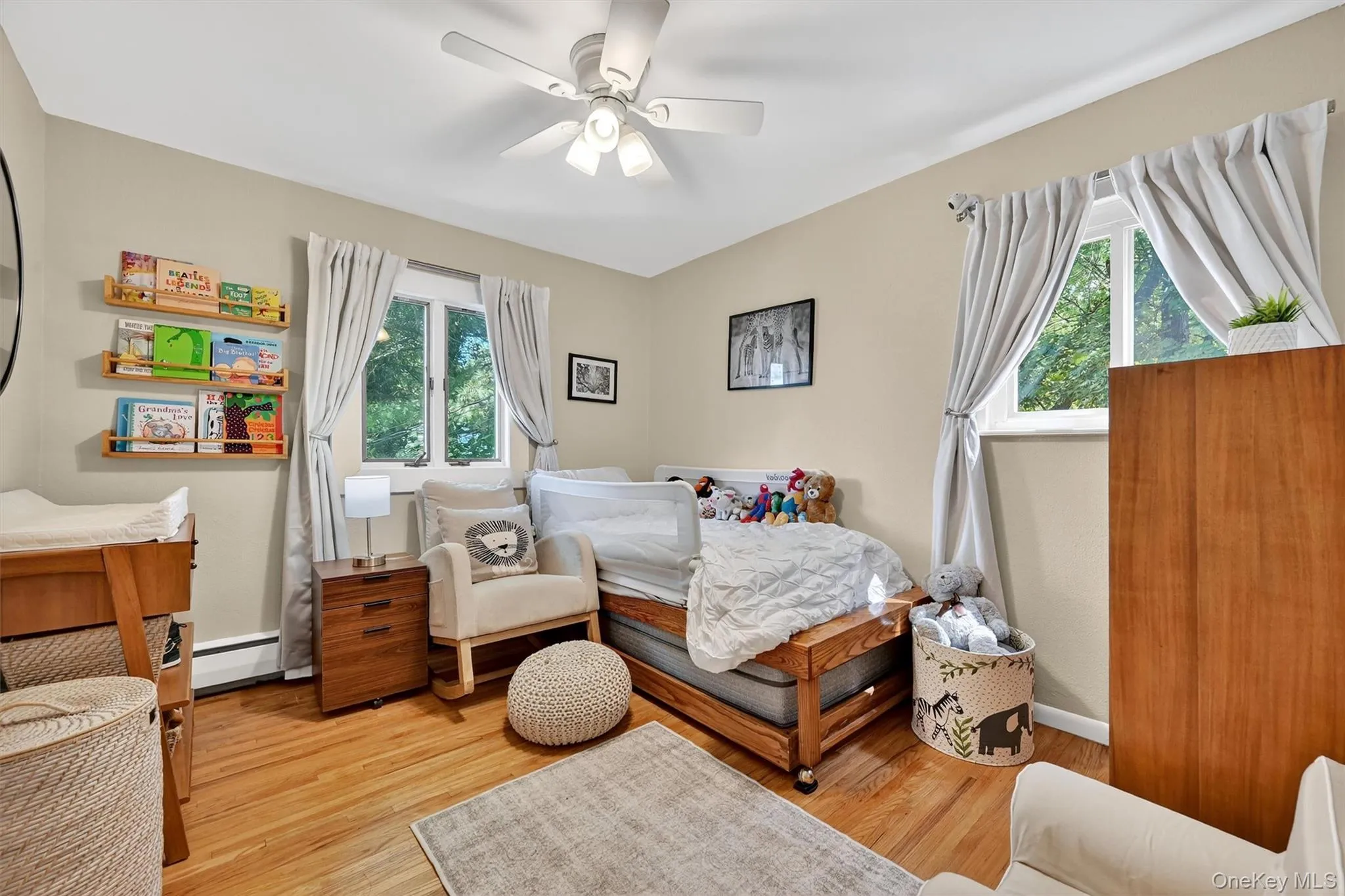 Bedroom featuring multiple windows, light wood-style flooring, ceiling fan, and baseboard heating Bedroom featuring multiple windows, light wood-style flooring, ceiling fan, and baseboard heating